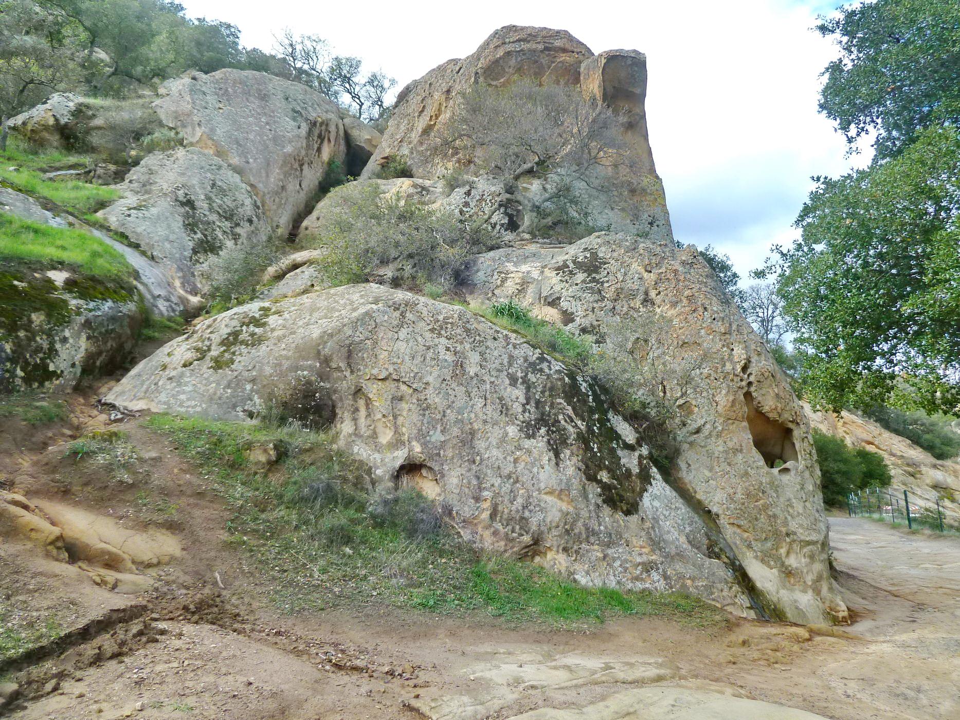 Large, weathered rock formations on a grassy slope under a bright sky.