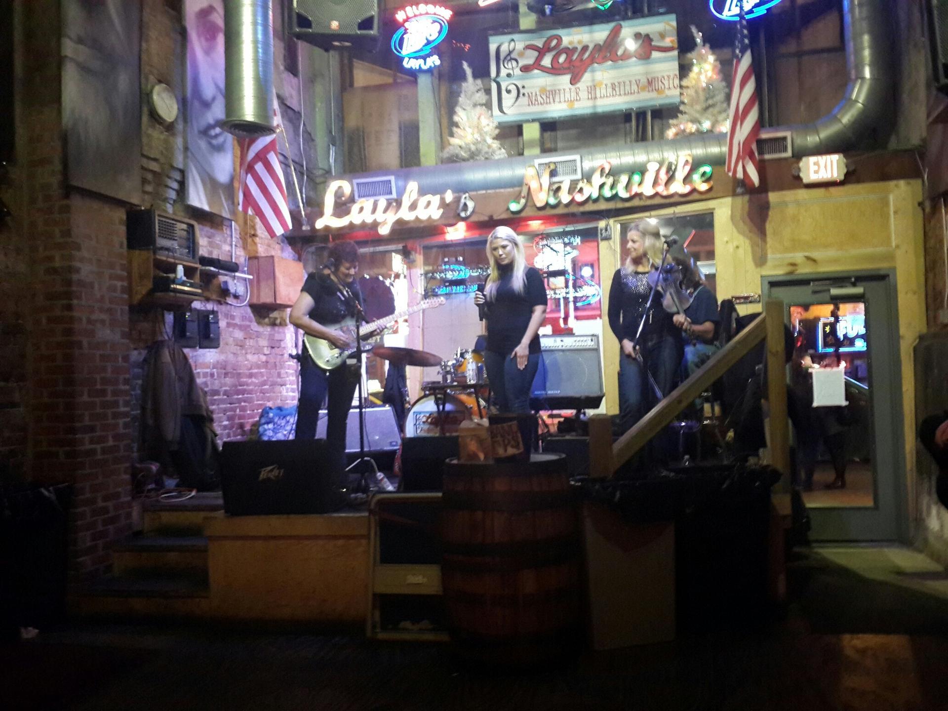 A band performs on a dimly lit stage inside a lively bar.