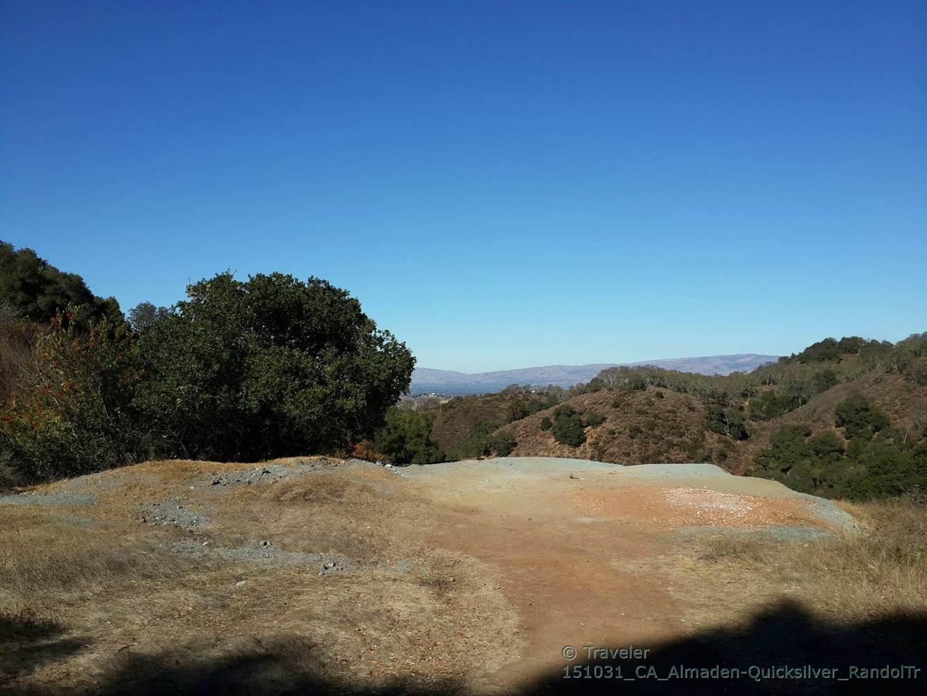 Open dirt clearing surrounded by trees, with distant hills under clear sky.