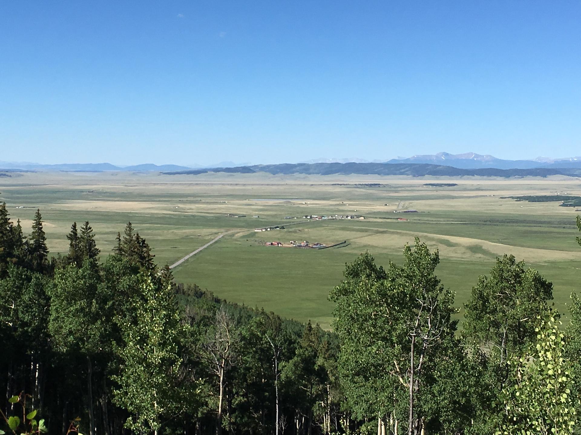 Vast green valley with distant mountains under a clear blue sky.