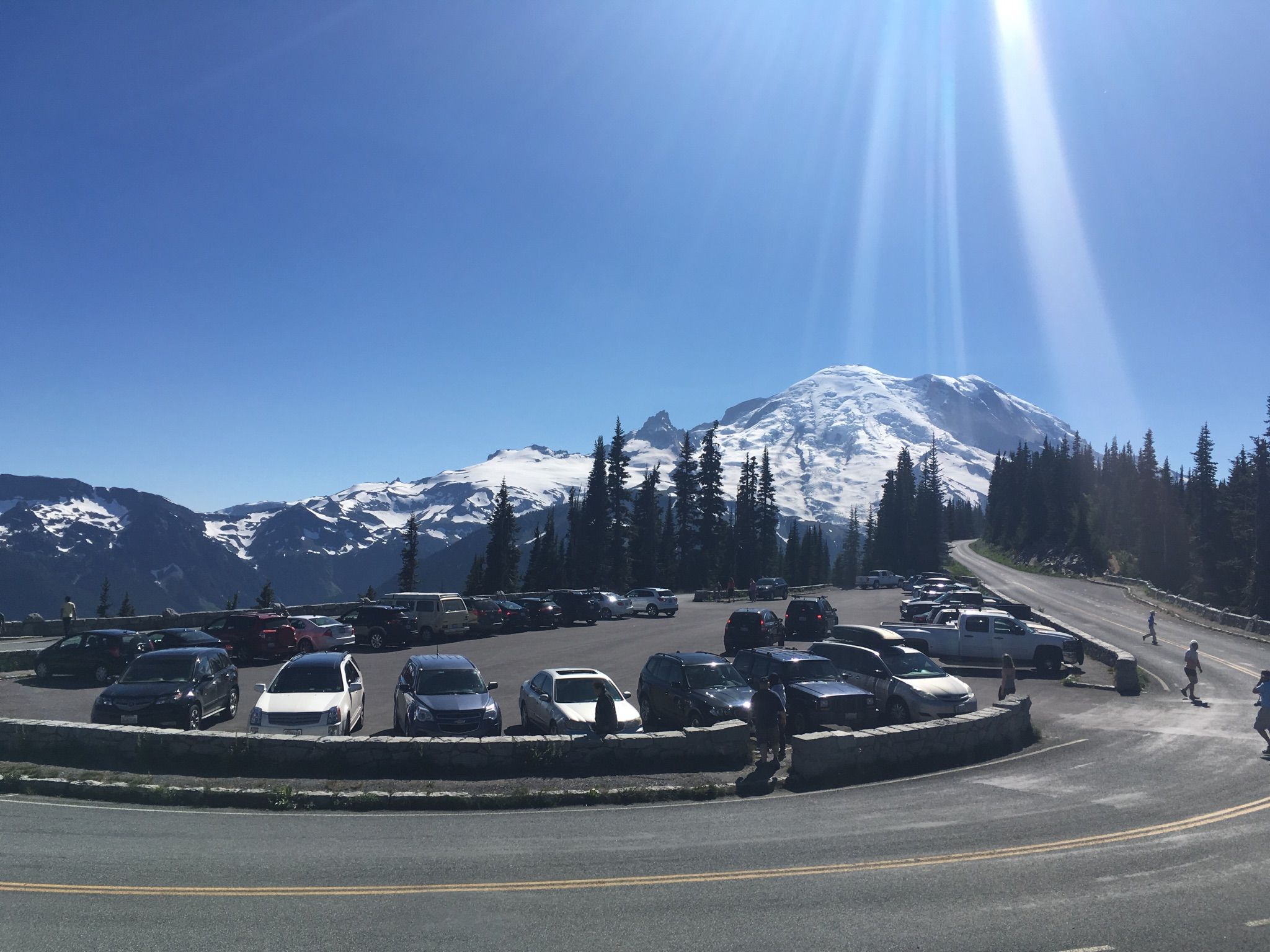 A parking lot full of cars with a large snow-capped mountain under bright sun. - Sunrise Park Road