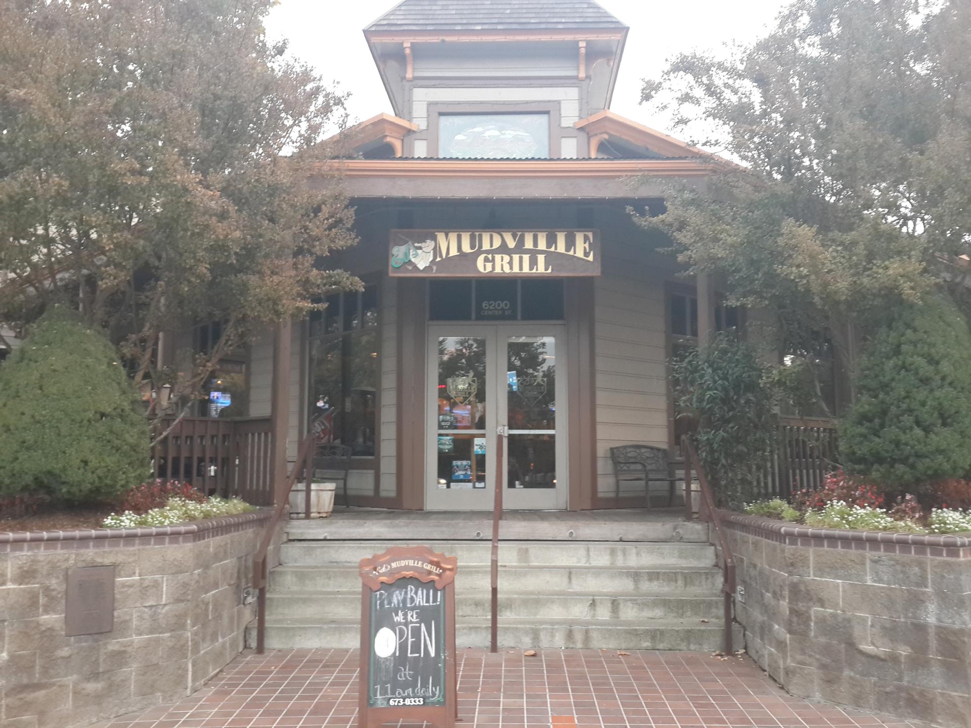 Front entrance of a building named 'Mudville Grill' on an overcast day.