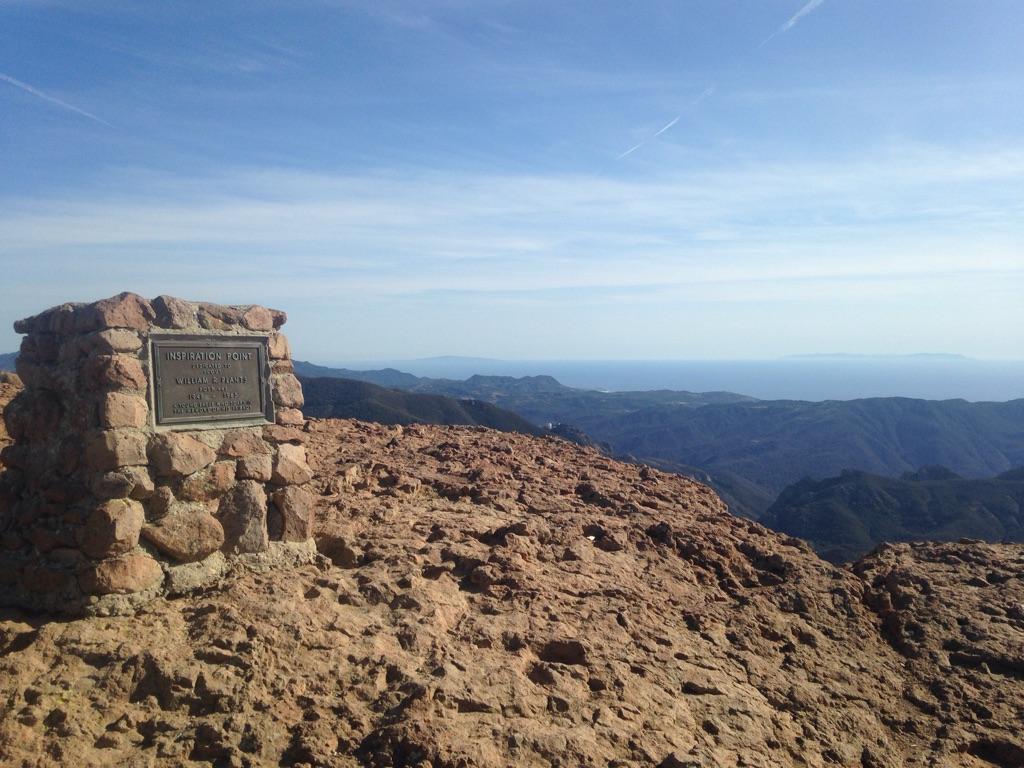 Stone monument on a rocky peak overlooking distant mountains and ocean.