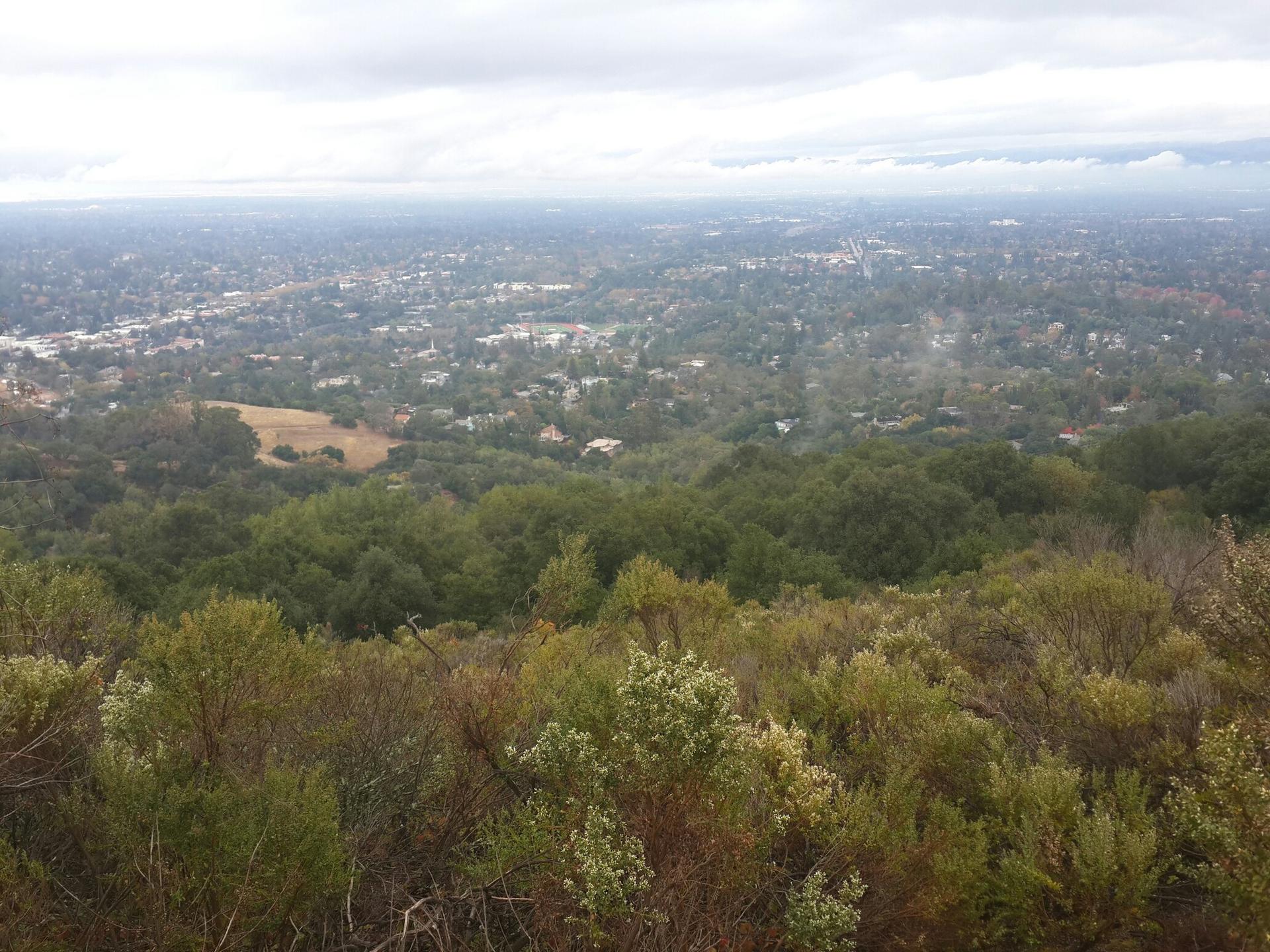 Overcast view of a distant town nestled among green hills.