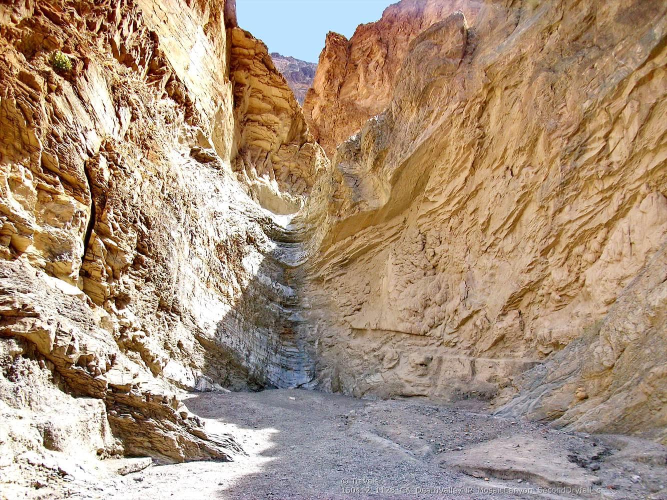 Deep, narrow slot canyon with towering, textured rock walls and bright light.