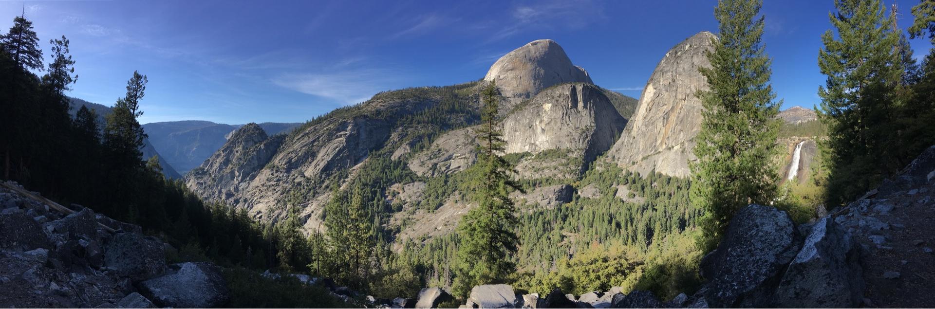 Panoramic view of majestic granite mountains, dense forest, and a distant waterfall.