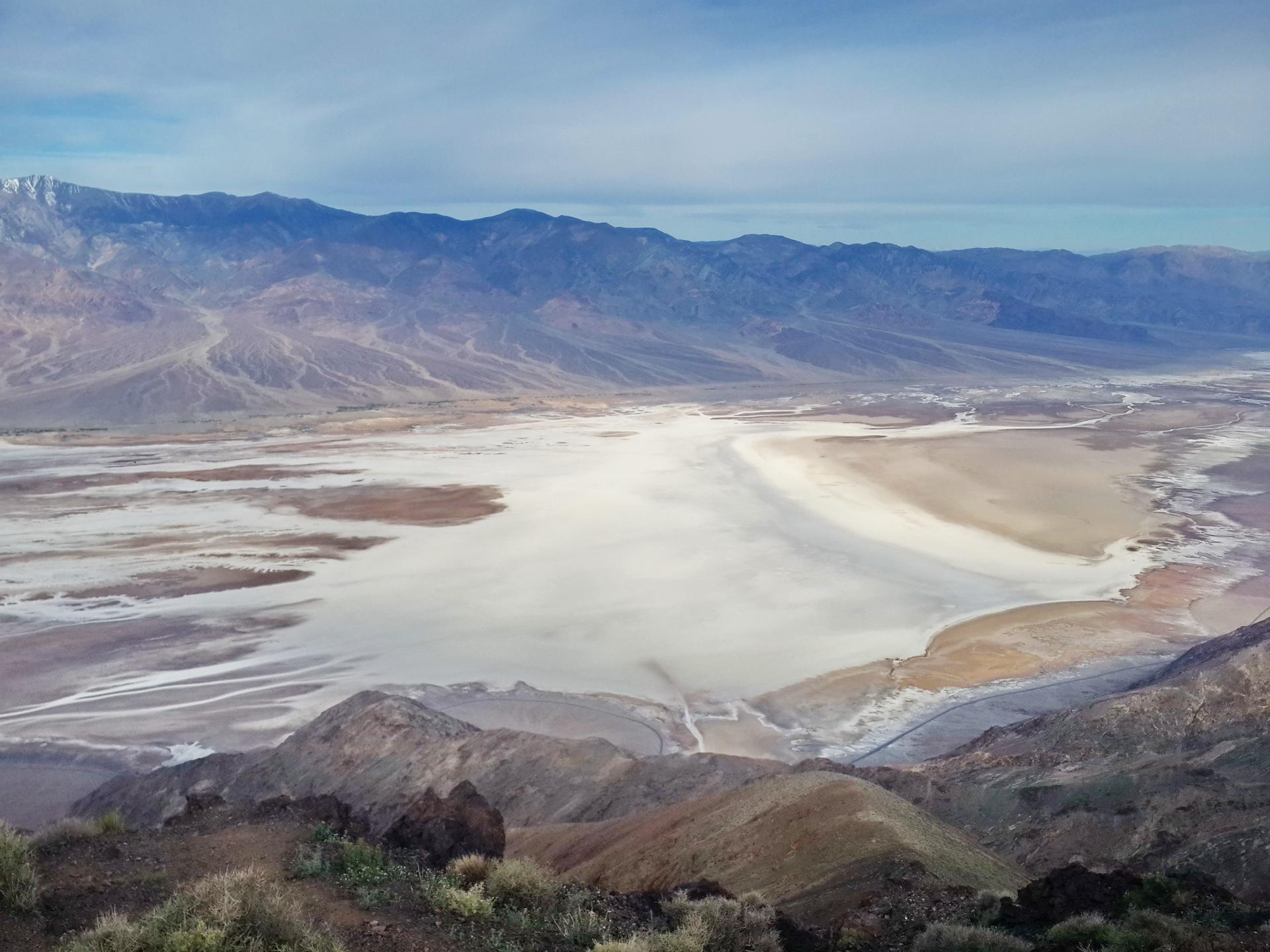 Expansive desert valley with a white salt flat under a bright blue sky.