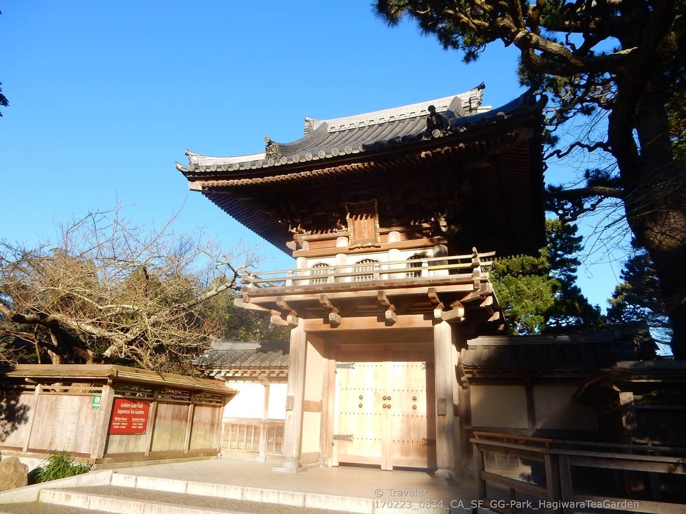 An ornate wooden temple gate with a tiered roof under a bright blue sky.
