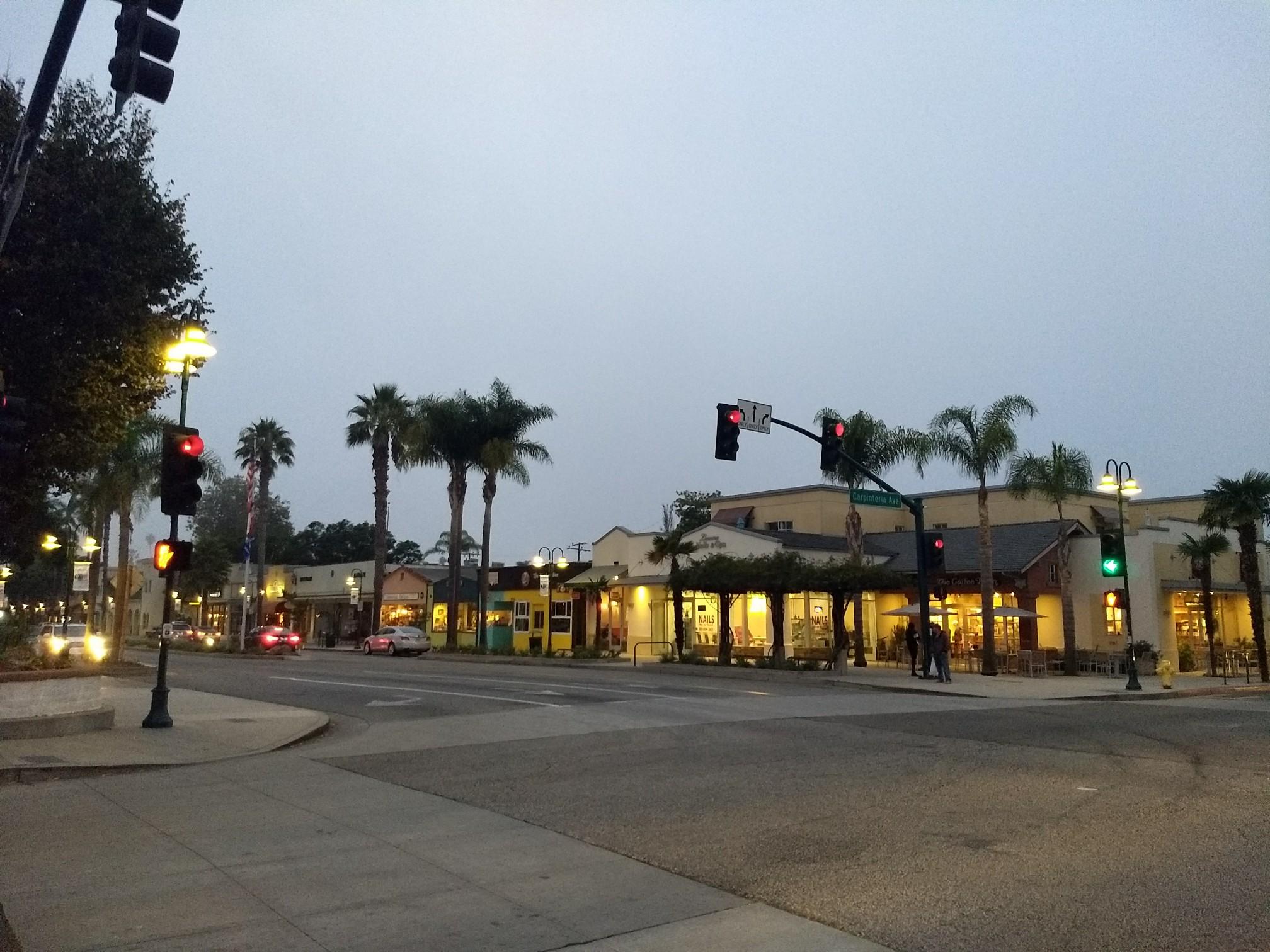 City street with palm trees and illuminated buildings at dusk.