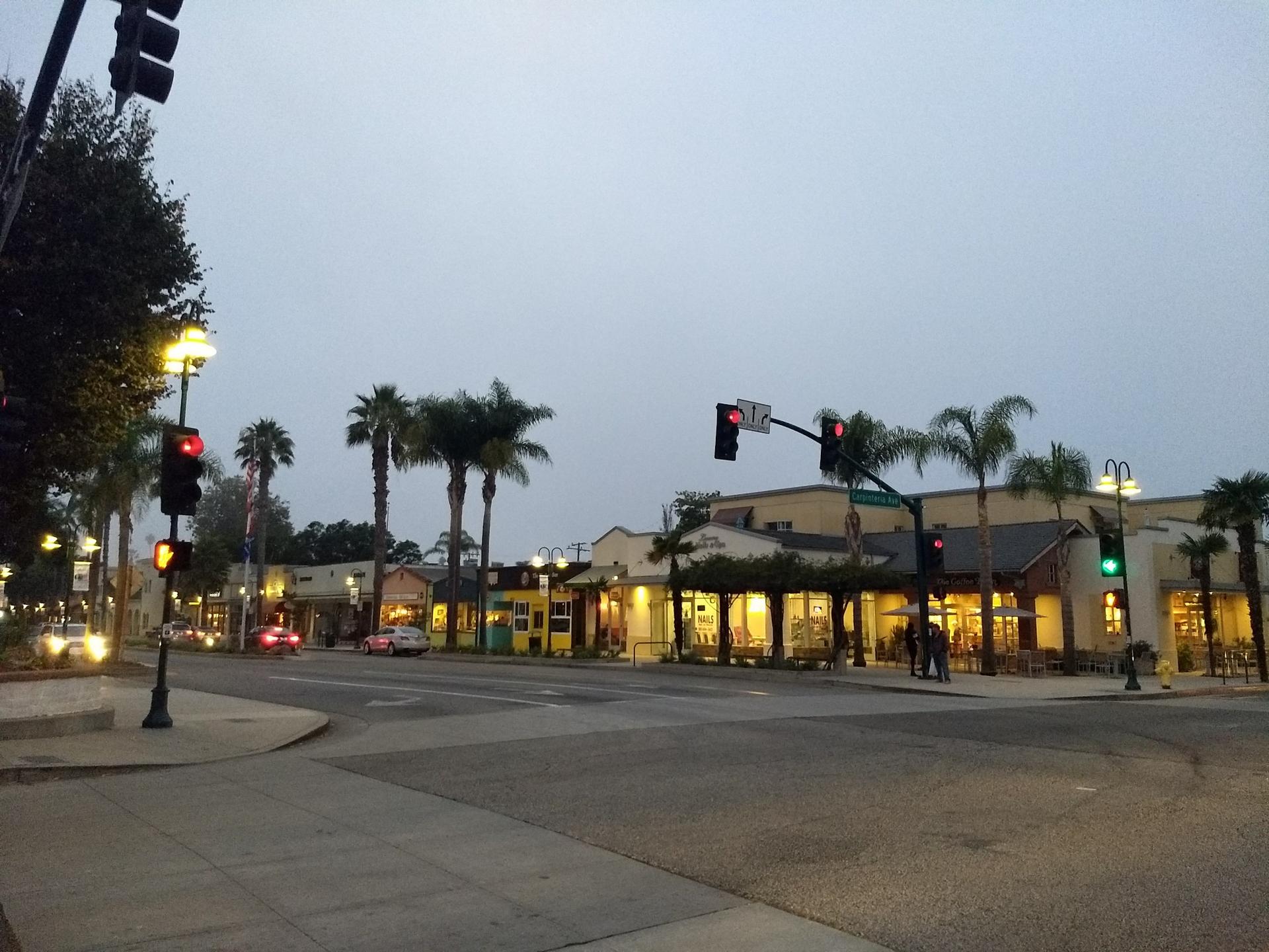 City street with palm trees and illuminated buildings at dusk.