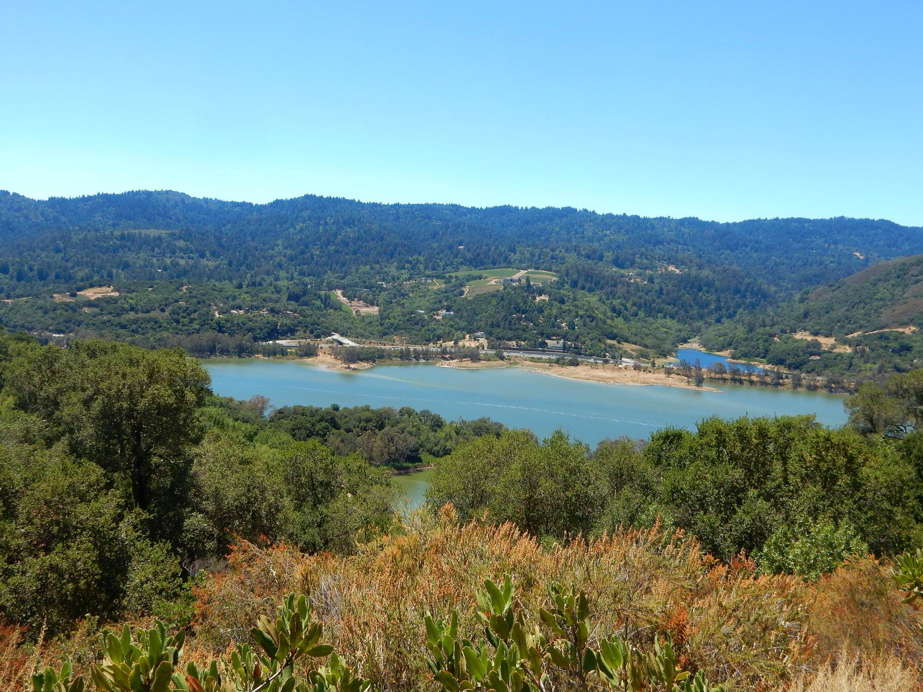 A large blue lake nestled among green, forested hills on a sunny day.