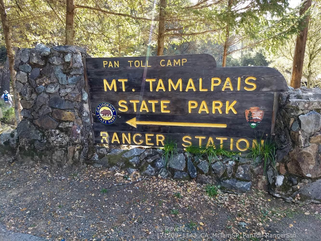 Large wooden sign with text and arrows, flanked by stone pillars.