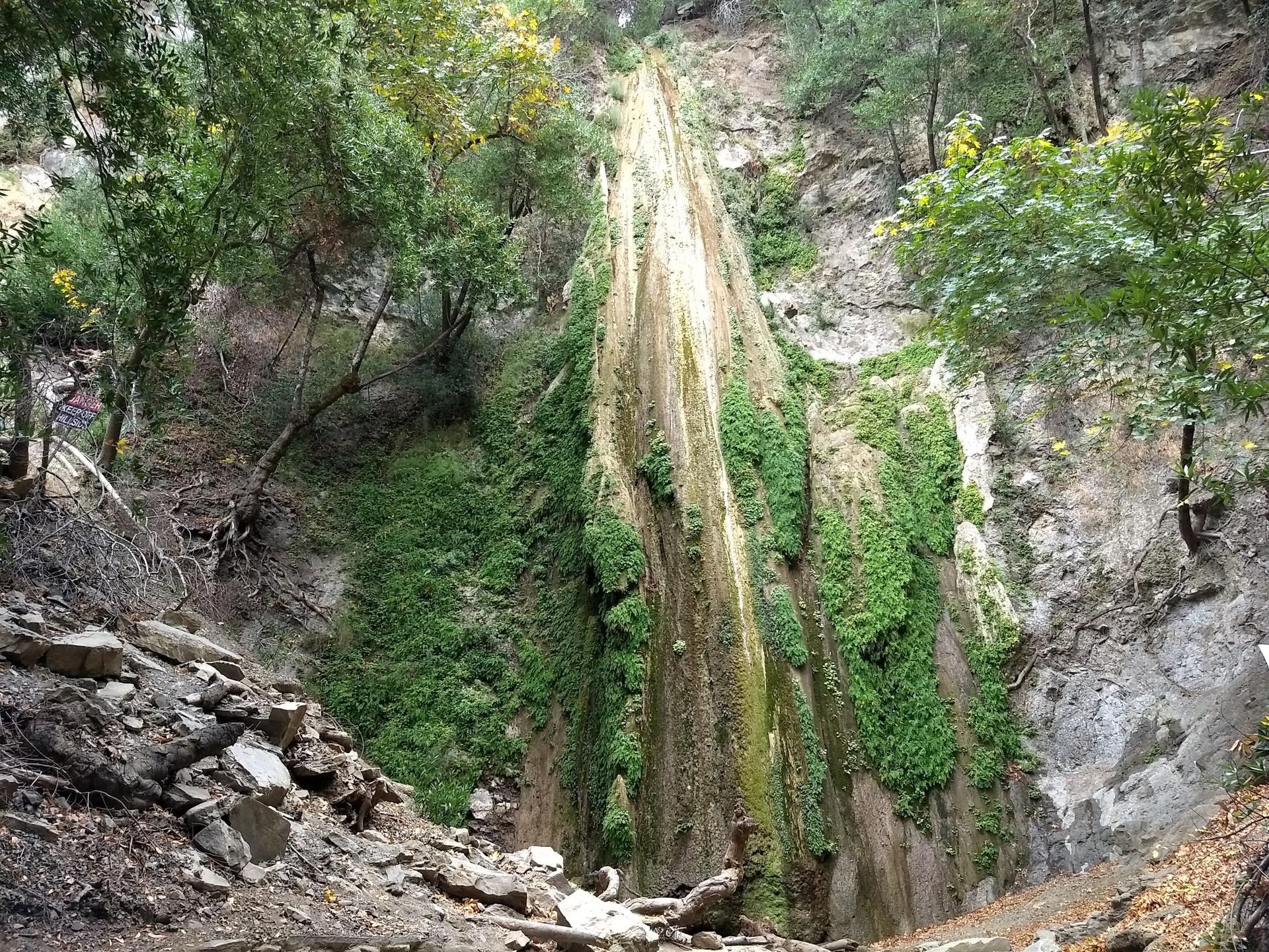 A tall, moss-covered waterfall cascades down a rocky cliff in a green forest.