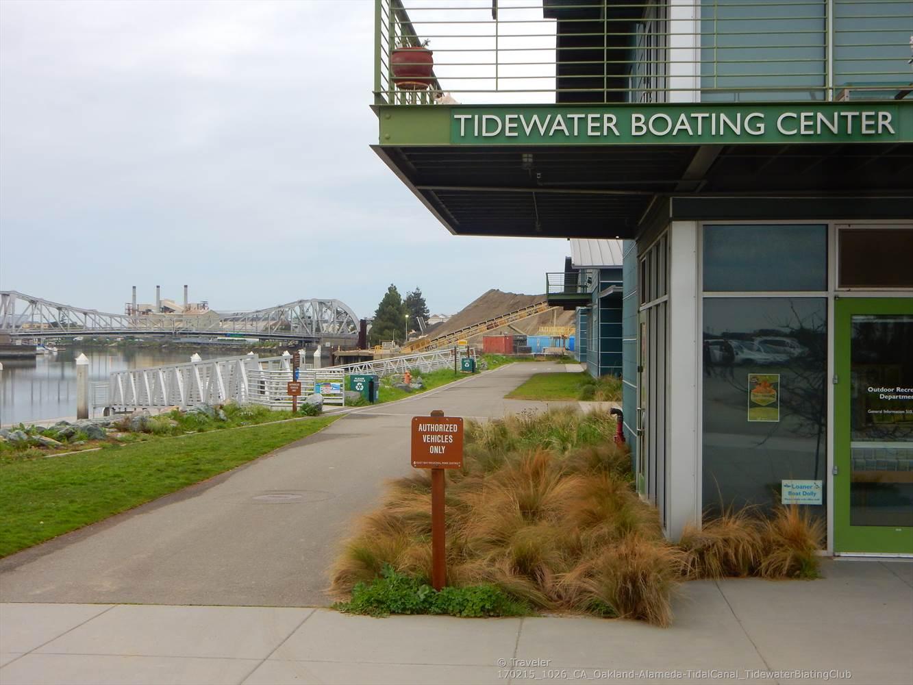 Modern building, paved path, and water with a distant bridge, overcast light.