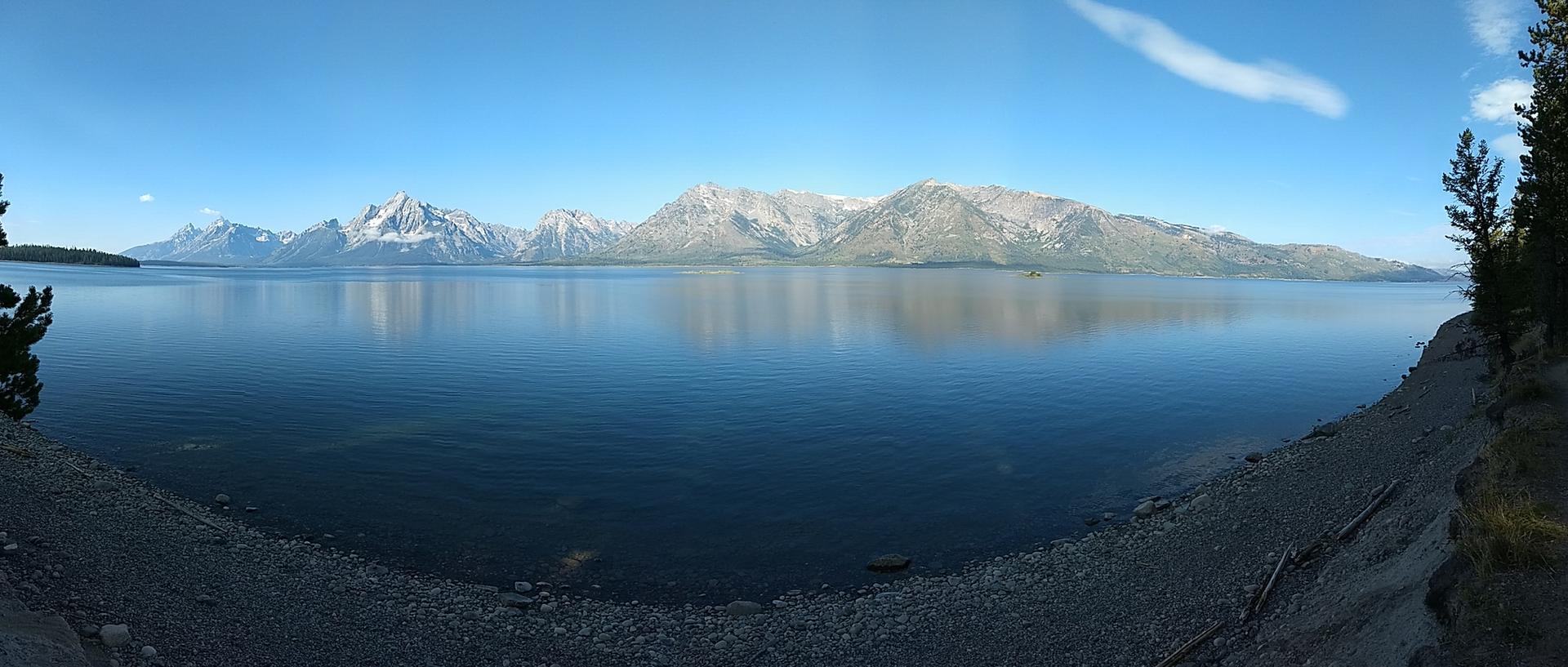 Panoramic blue lake with distant snow-capped mountains under a clear sky.