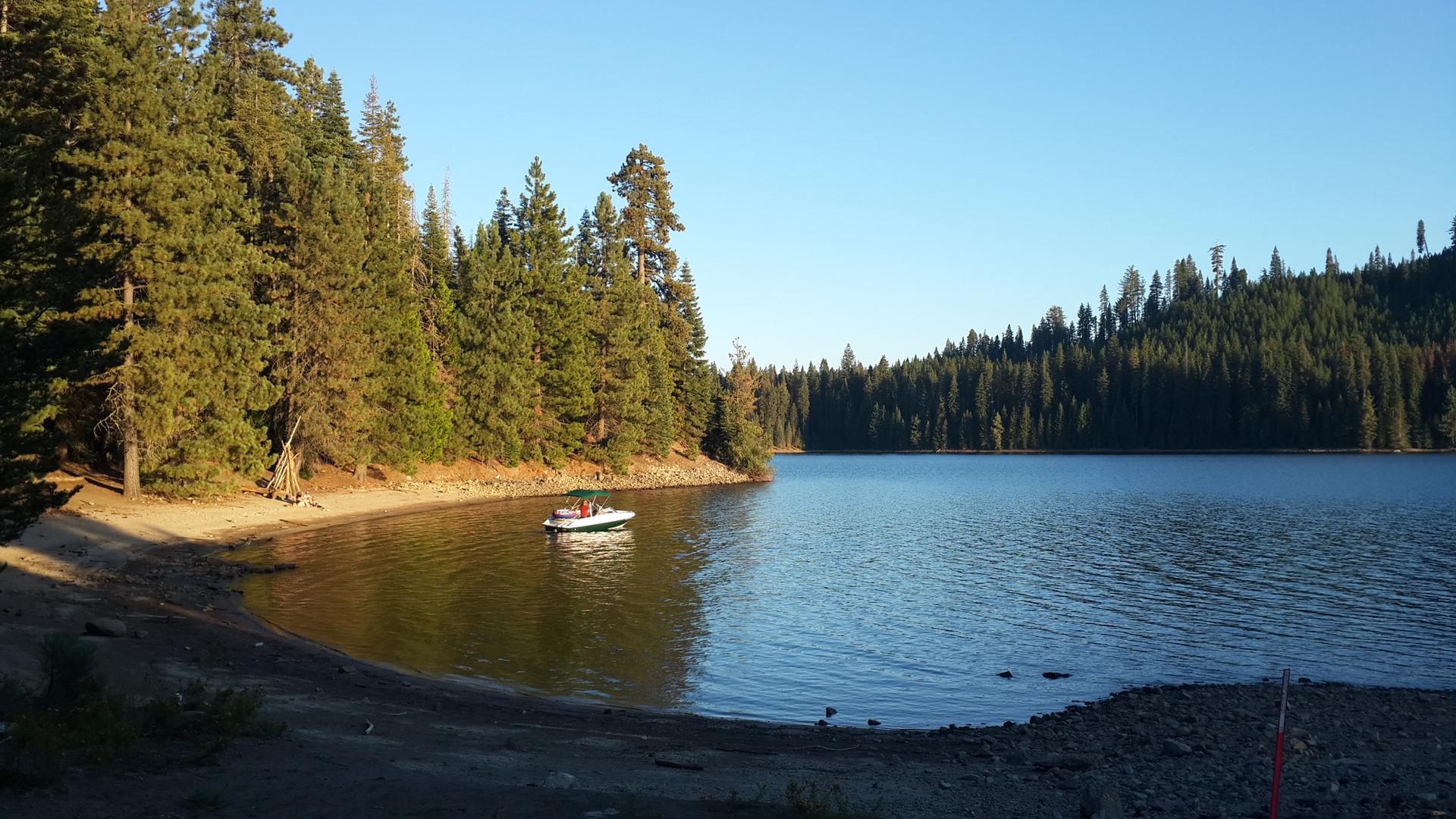 A small boat with people on a calm lake surrounded by pine trees.