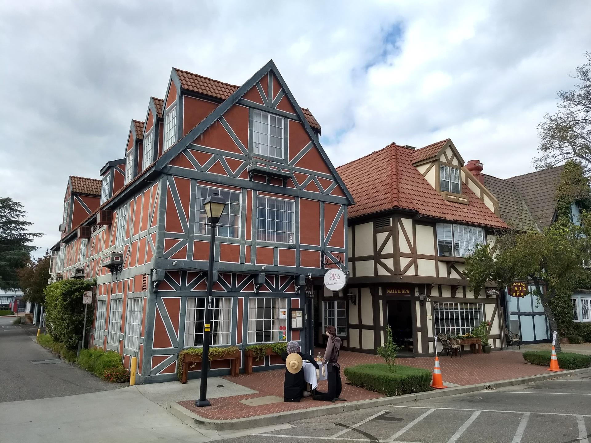 Ornate timber-framed buildings with people on the sidewalk under a cloudy sky.