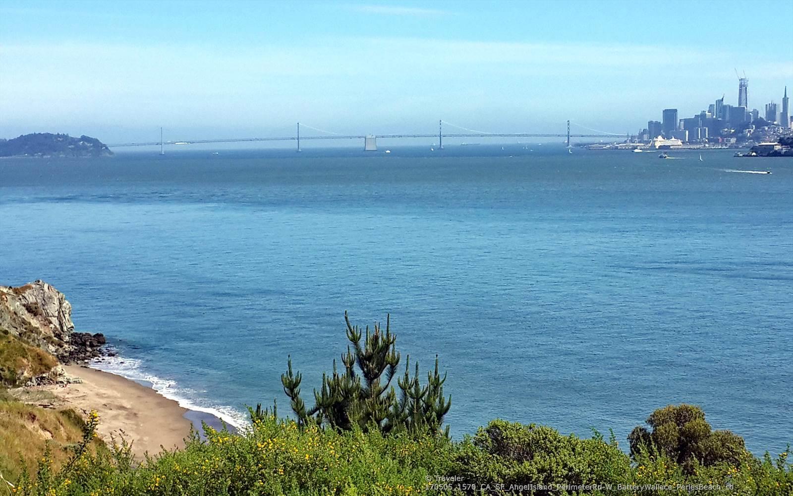 Coastal view of a small beach, calm bay, distant bridge, and city.