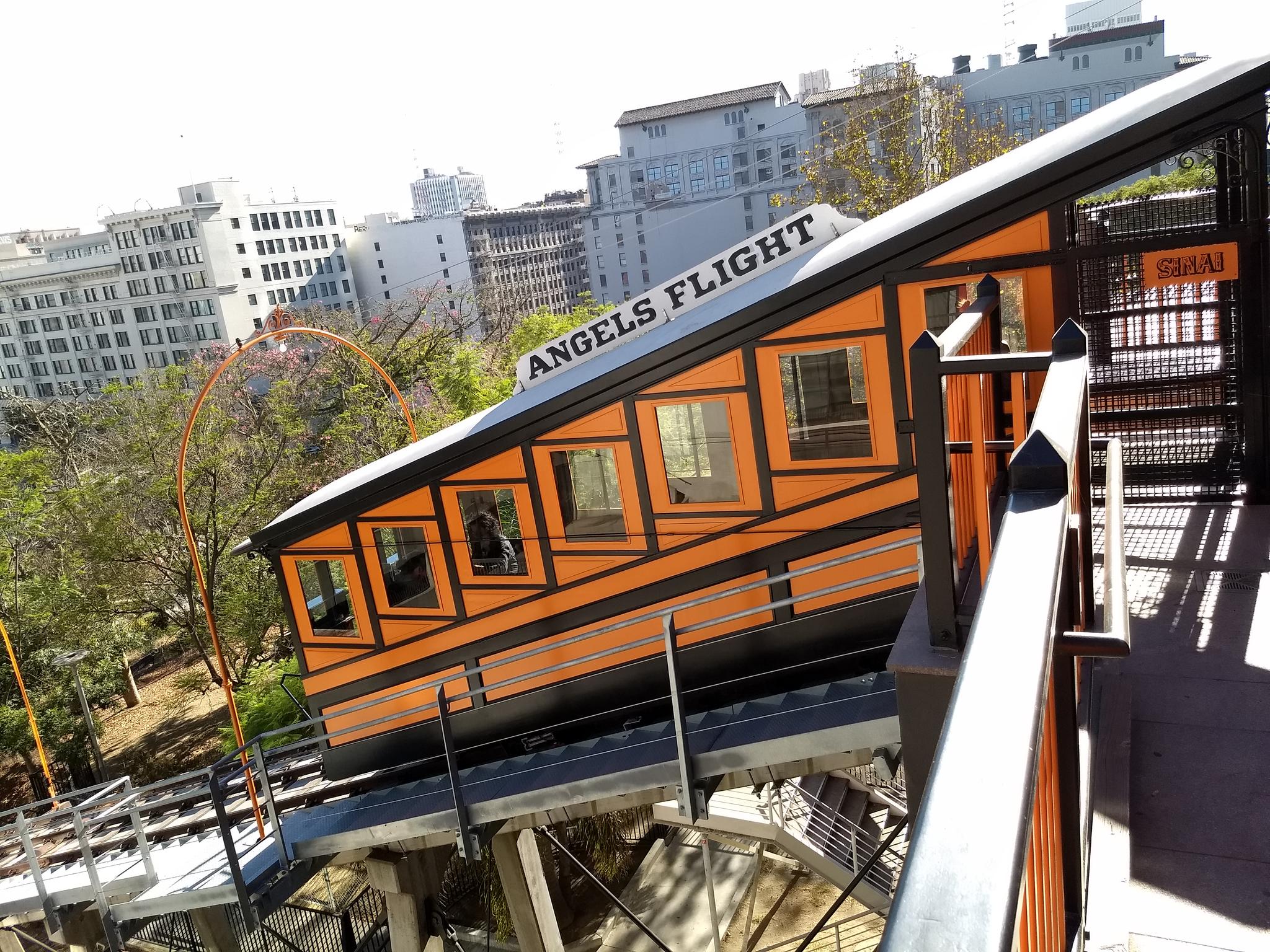 Orange and black funicular car on an incline, with city buildings behind.