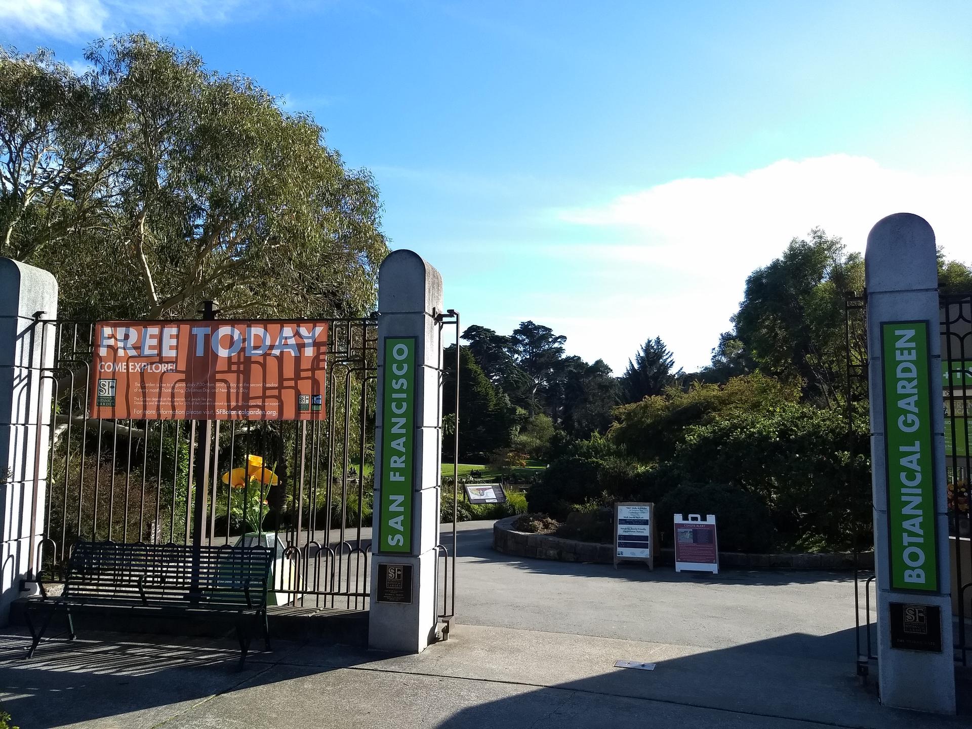 Large open gates to a botanical garden under a bright blue sky.