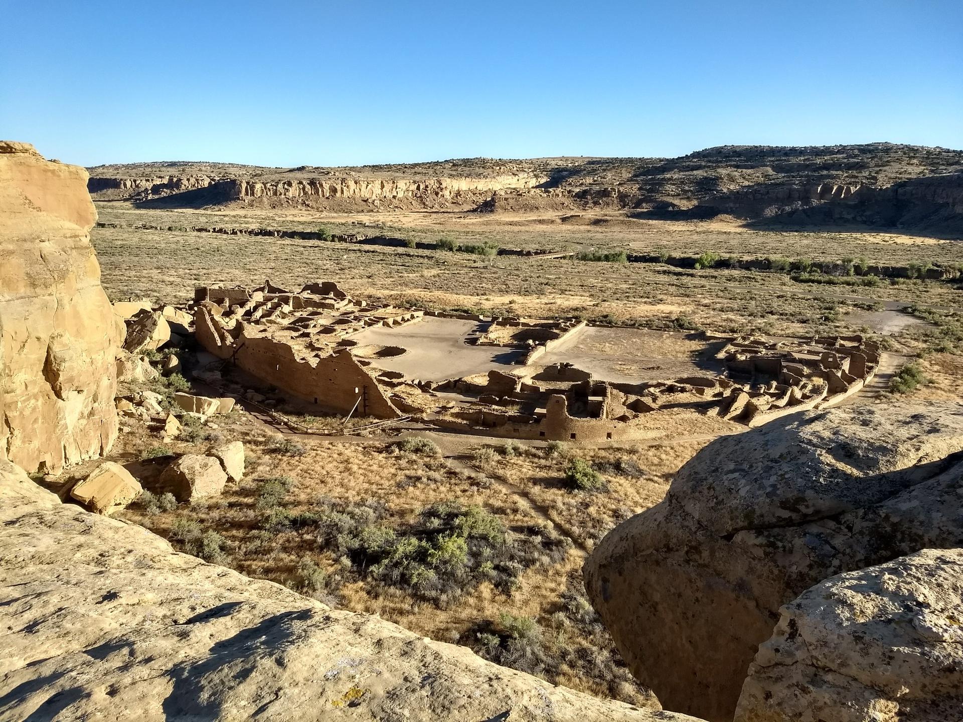 Overhead view of ancient stone ruins in a vast desert valley under clear sky.