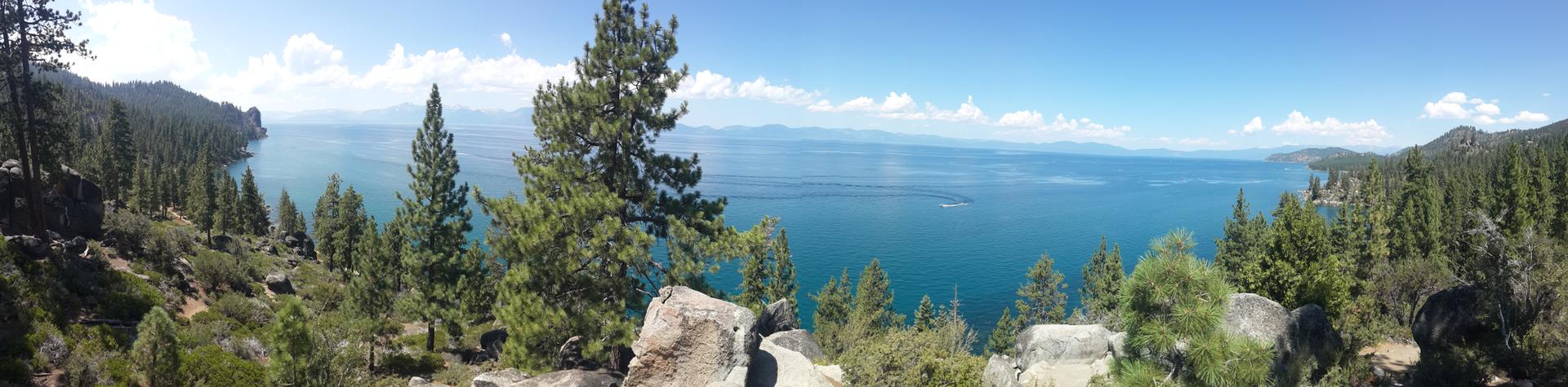 Panoramic view of a vast blue lake surrounded by green forested hills.