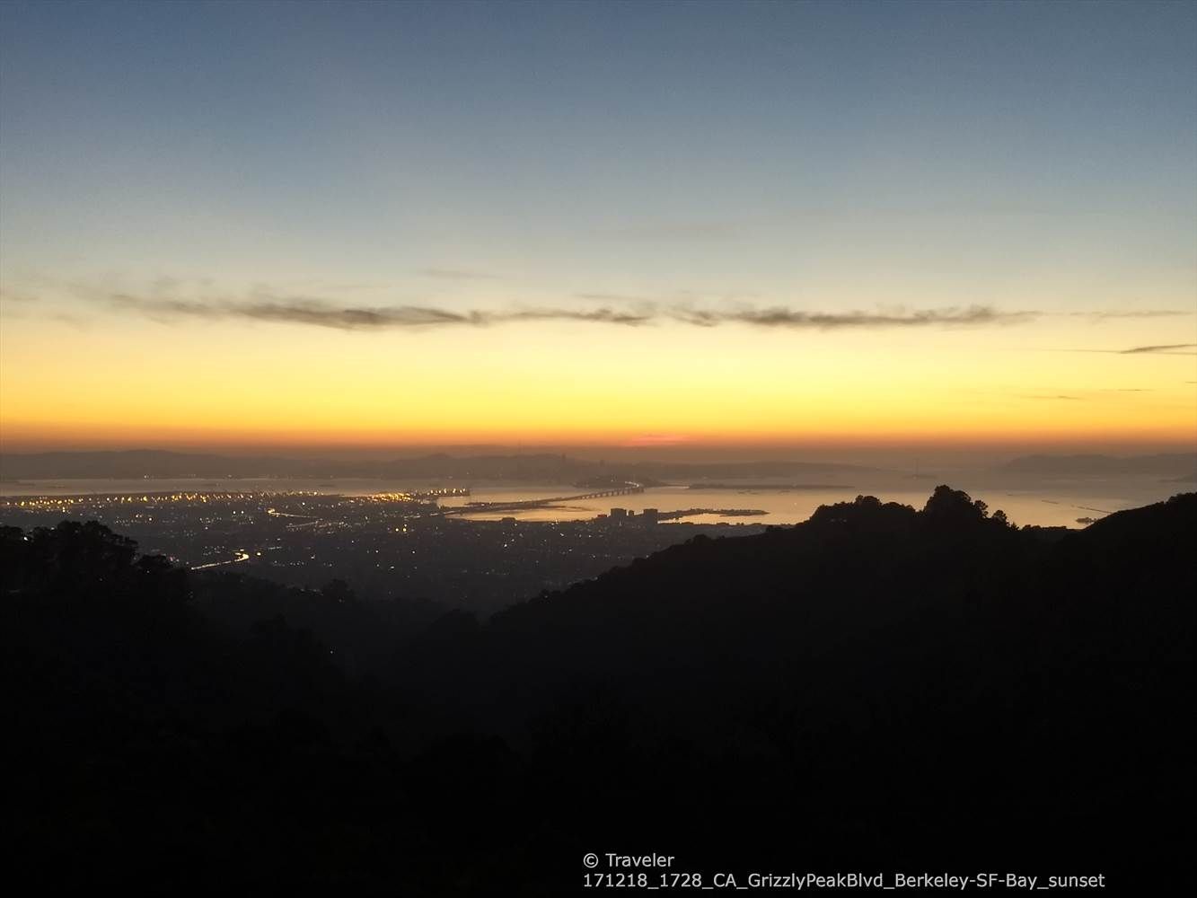 Panoramic sunset over a city and water, viewed from a dark hillside. - Grizzly Peak Loop