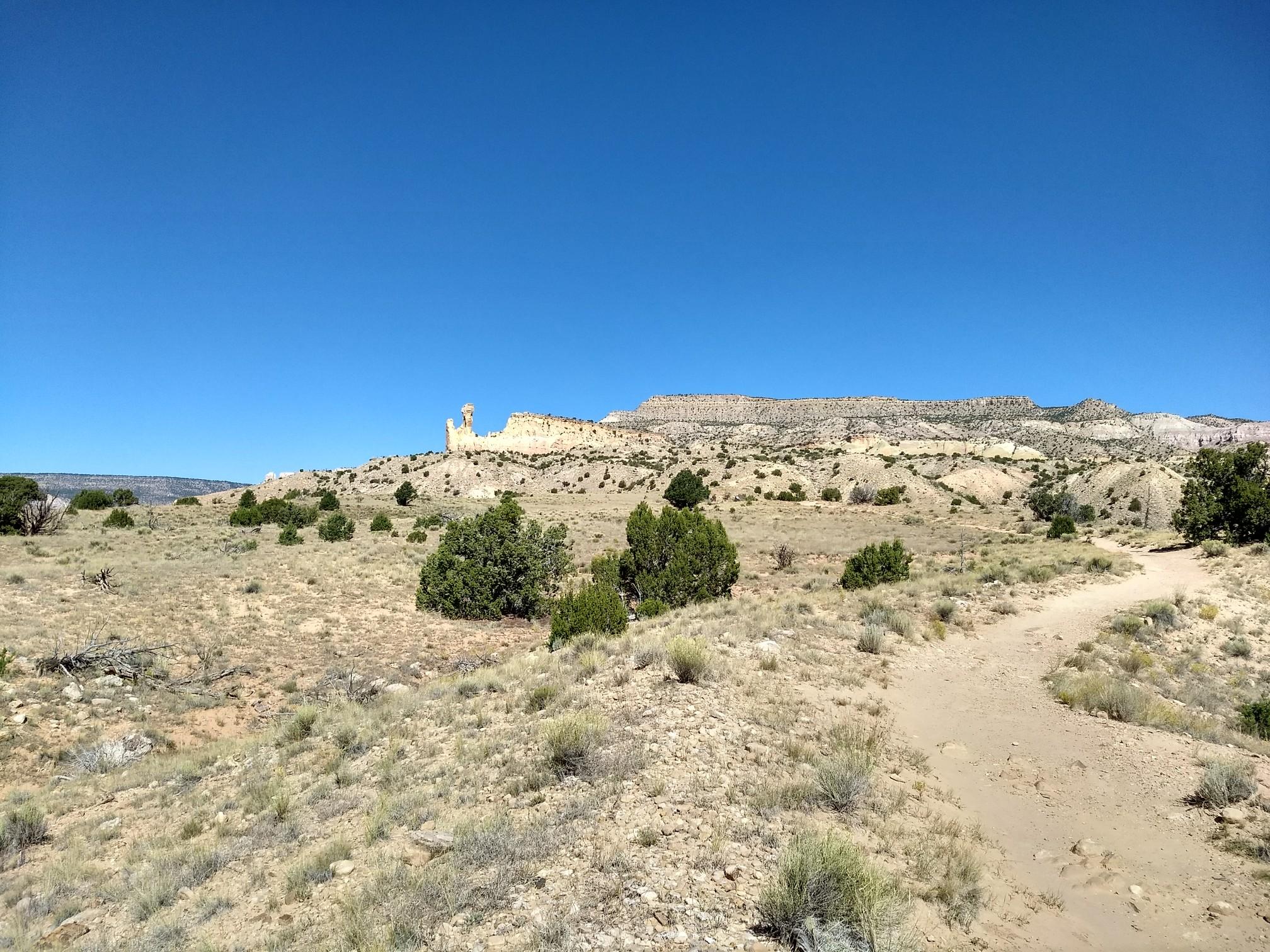 A desert path leads towards a distinctive rock formation under a clear sky.