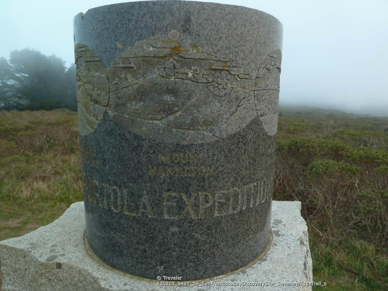 A cylindrical stone monument with carvings stands in a foggy, grassy landscape.