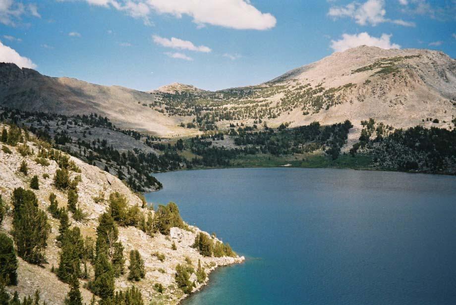 A large blue lake bordered by rocky, treed slopes under a partly cloudy sky.