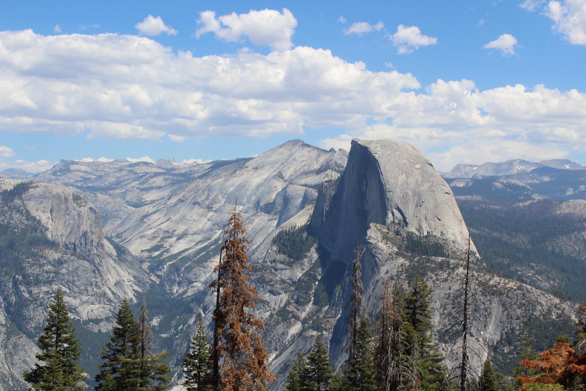 Majestic half-dome mountain dominates a vast, rugged landscape under a bright, cloudy sky.