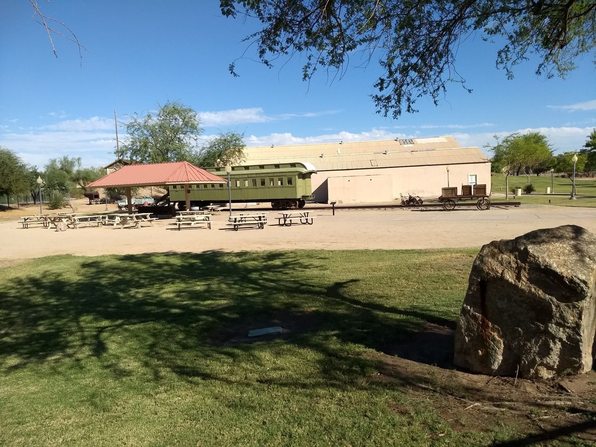 Green train car and picnic tables in a park-like setting on a sunny day. - East Main Canal Path Loop