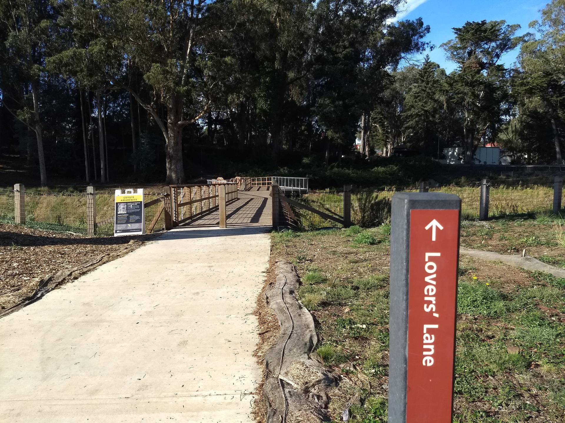 Paved path leading to a wooden bridge, with a signpost pointing right.