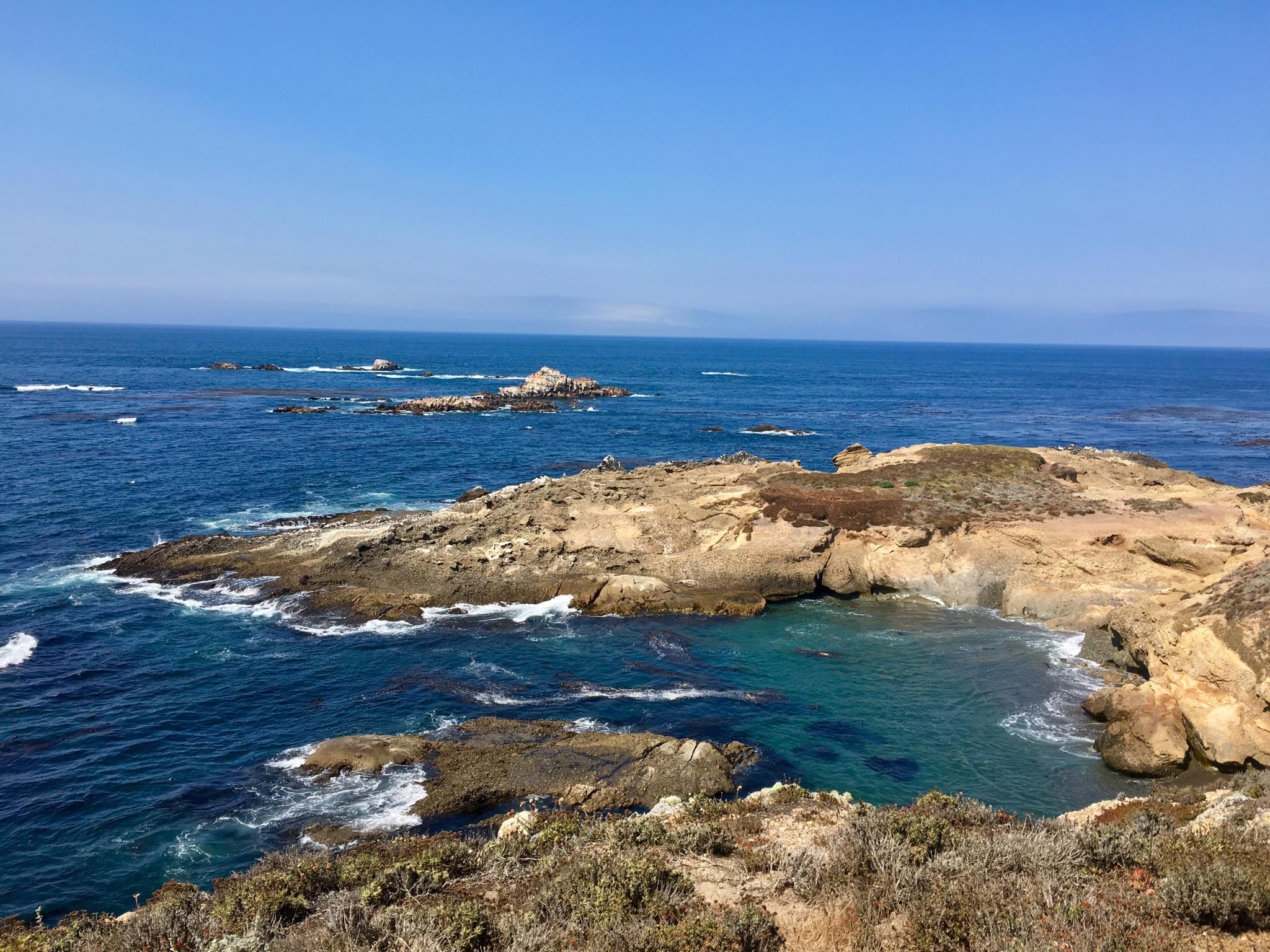Expansive blue ocean with rocky islands and a clear turquoise cove on a sunny day.