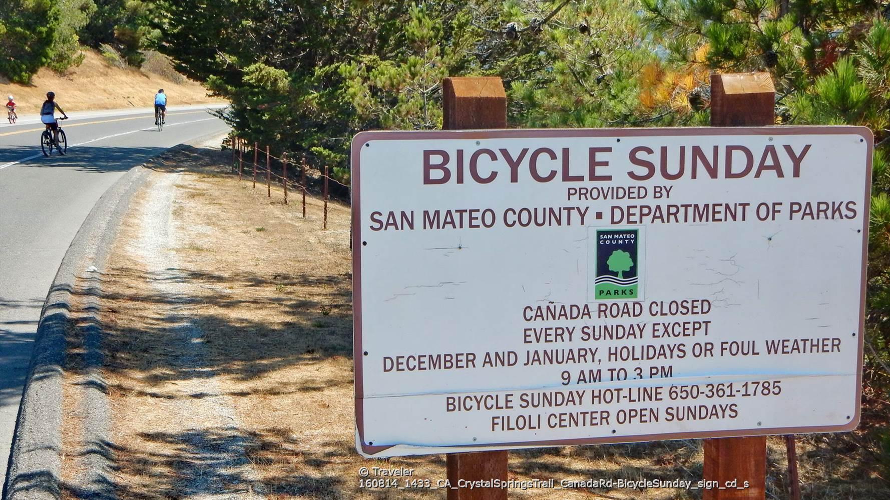 A sign for 'Bicycle Sunday' next to a road with cyclists.