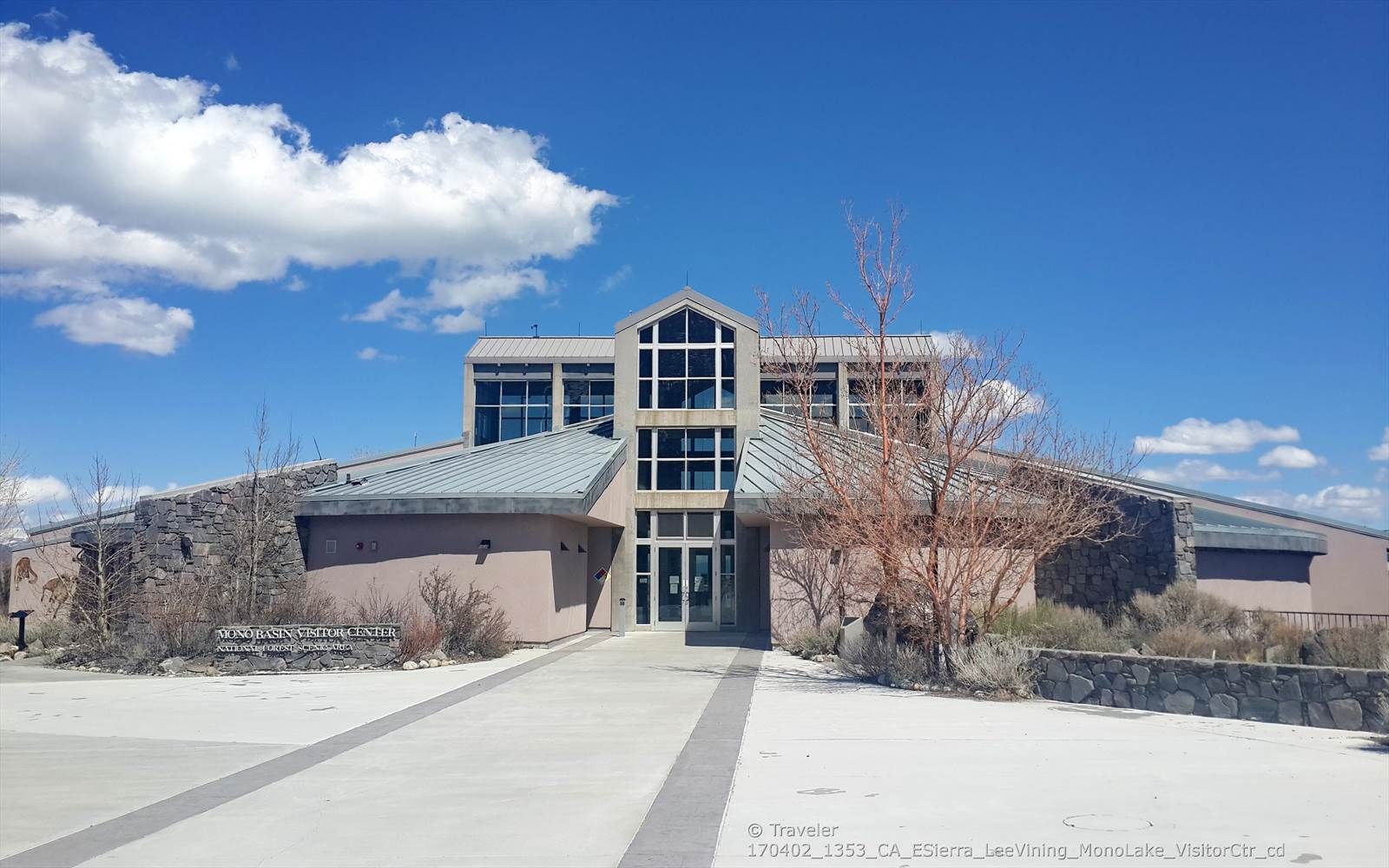 A modern building with large windows under a bright blue sky with white clouds. - Mono Lake Trail