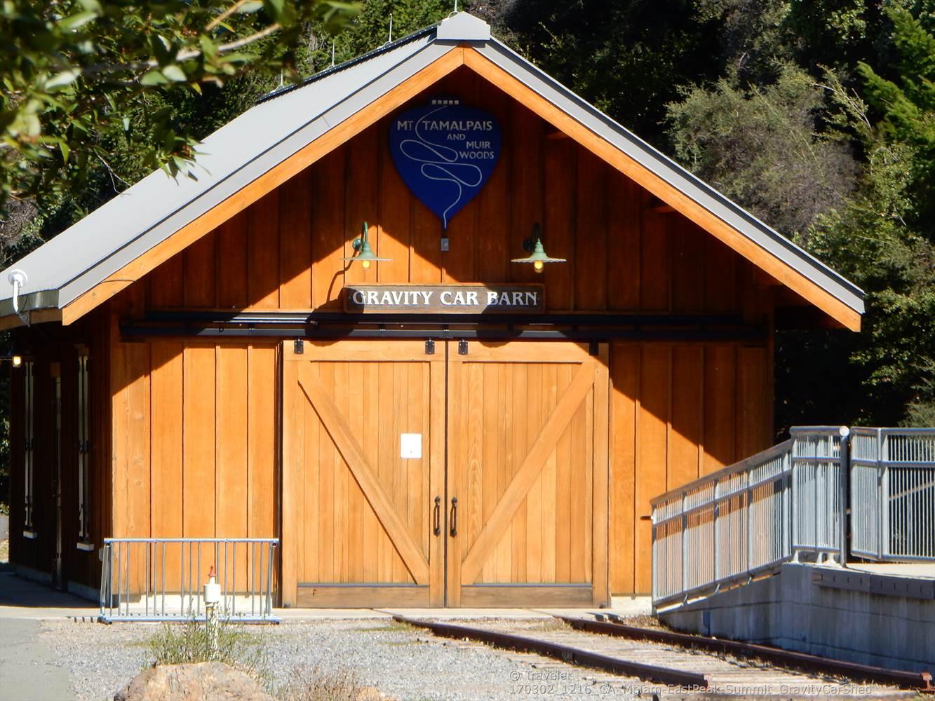 A rustic wooden barn with a 'Gravity Car Barn' sign on a sunny day.