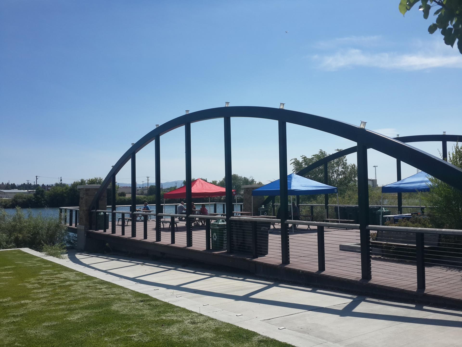 Arched metal bridge structure over a wooden deck with picnic tables.