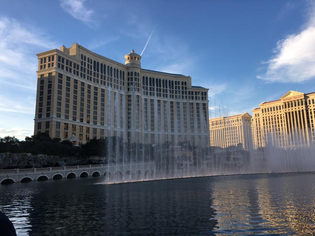 Grand building with fountains spraying water in a lake under a blue sky.