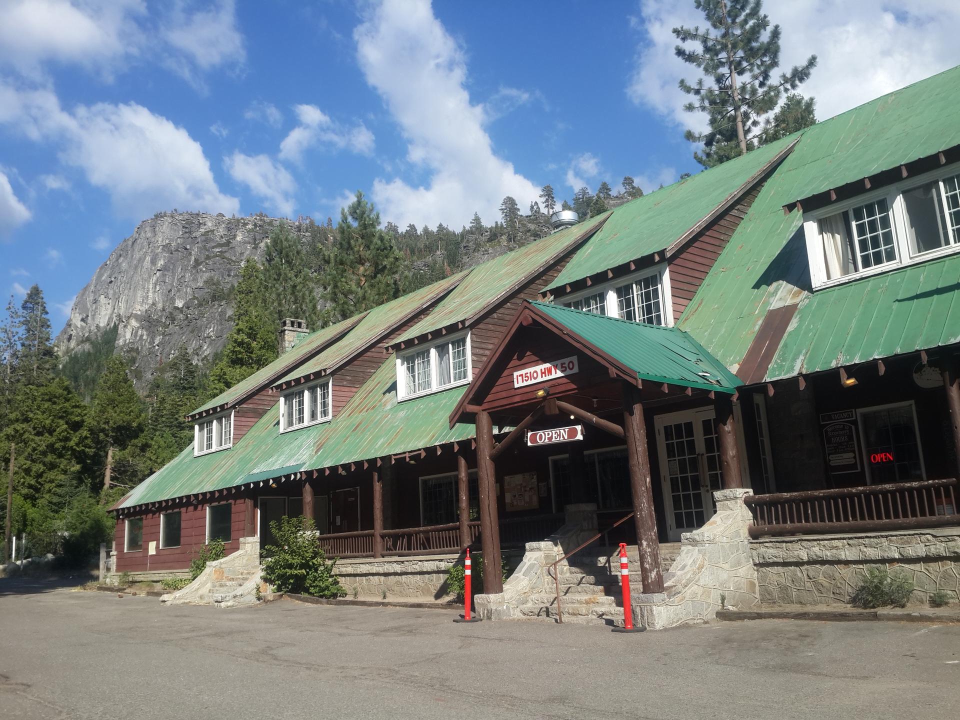 A large lodge with a green roof stands against a rocky mountain.