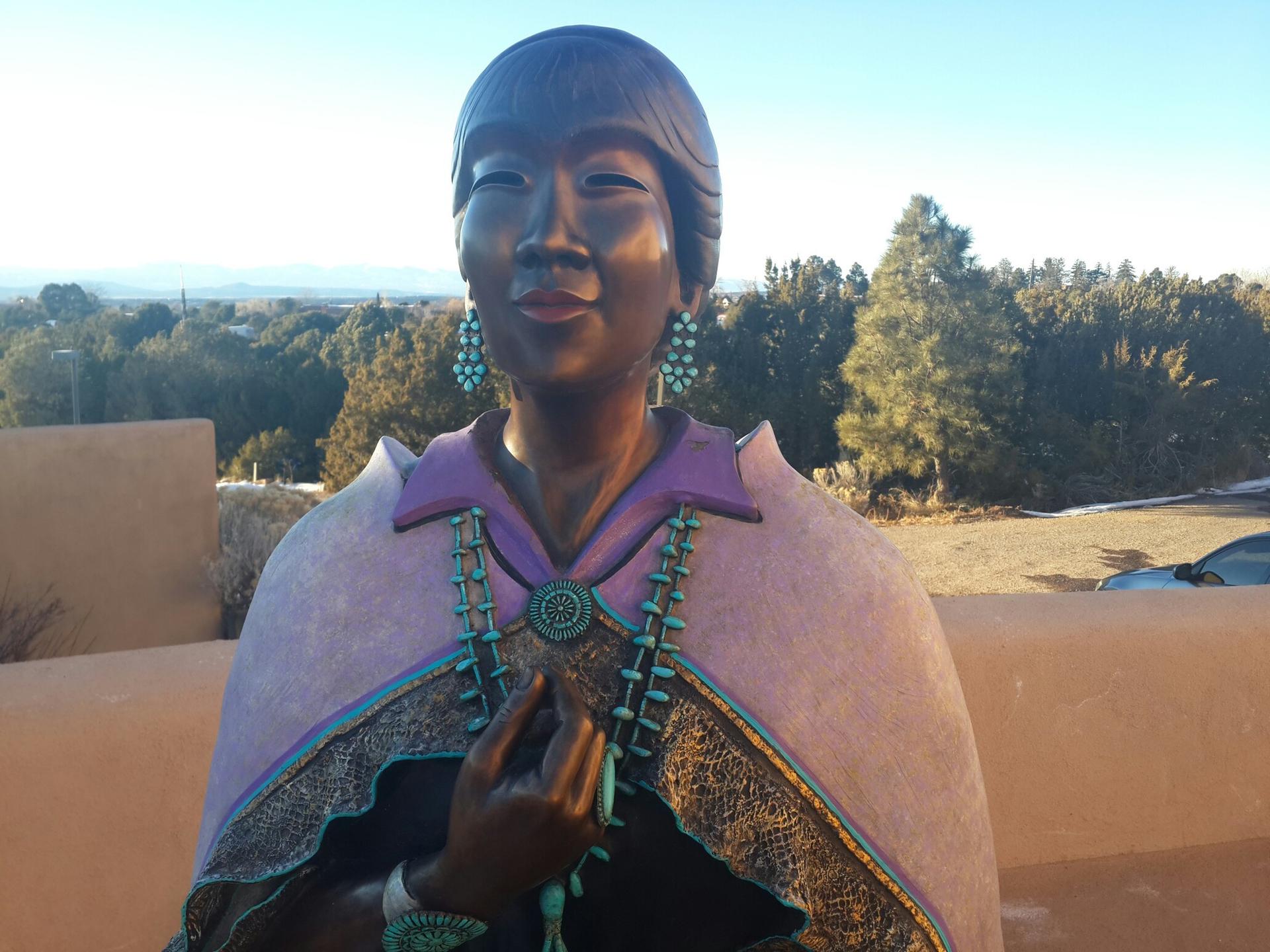 Bronze statue of a woman wearing turquoise jewelry, bathed in golden light.