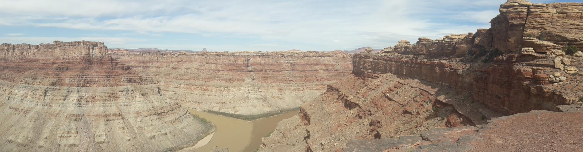 Panoramic view of a vast canyon with a river confluence below, under a hazy sky.
