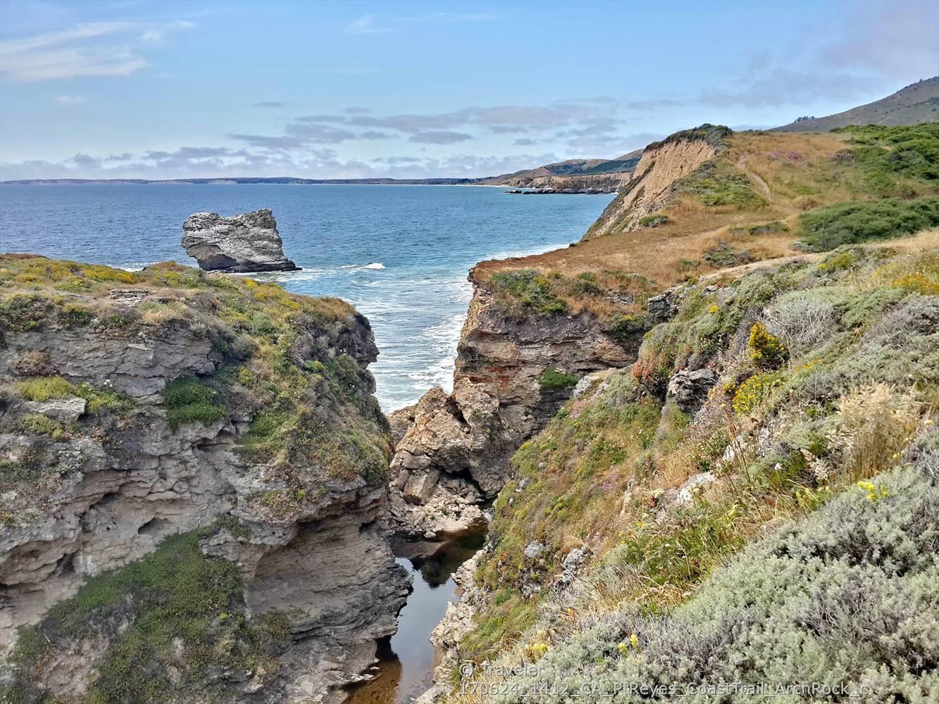 Rugged coastal cliffs overlook a blue ocean with a large sea stack.