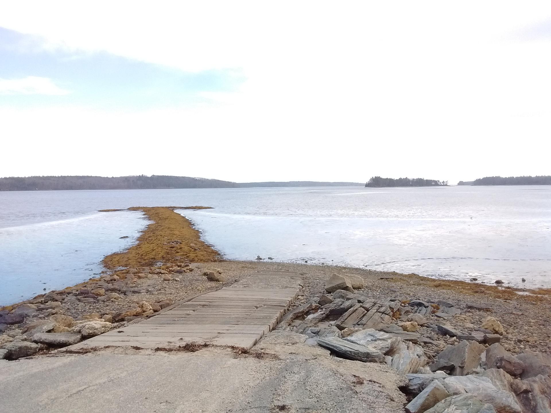 Wooden ramp and rocky path extending into a wide body of water.
