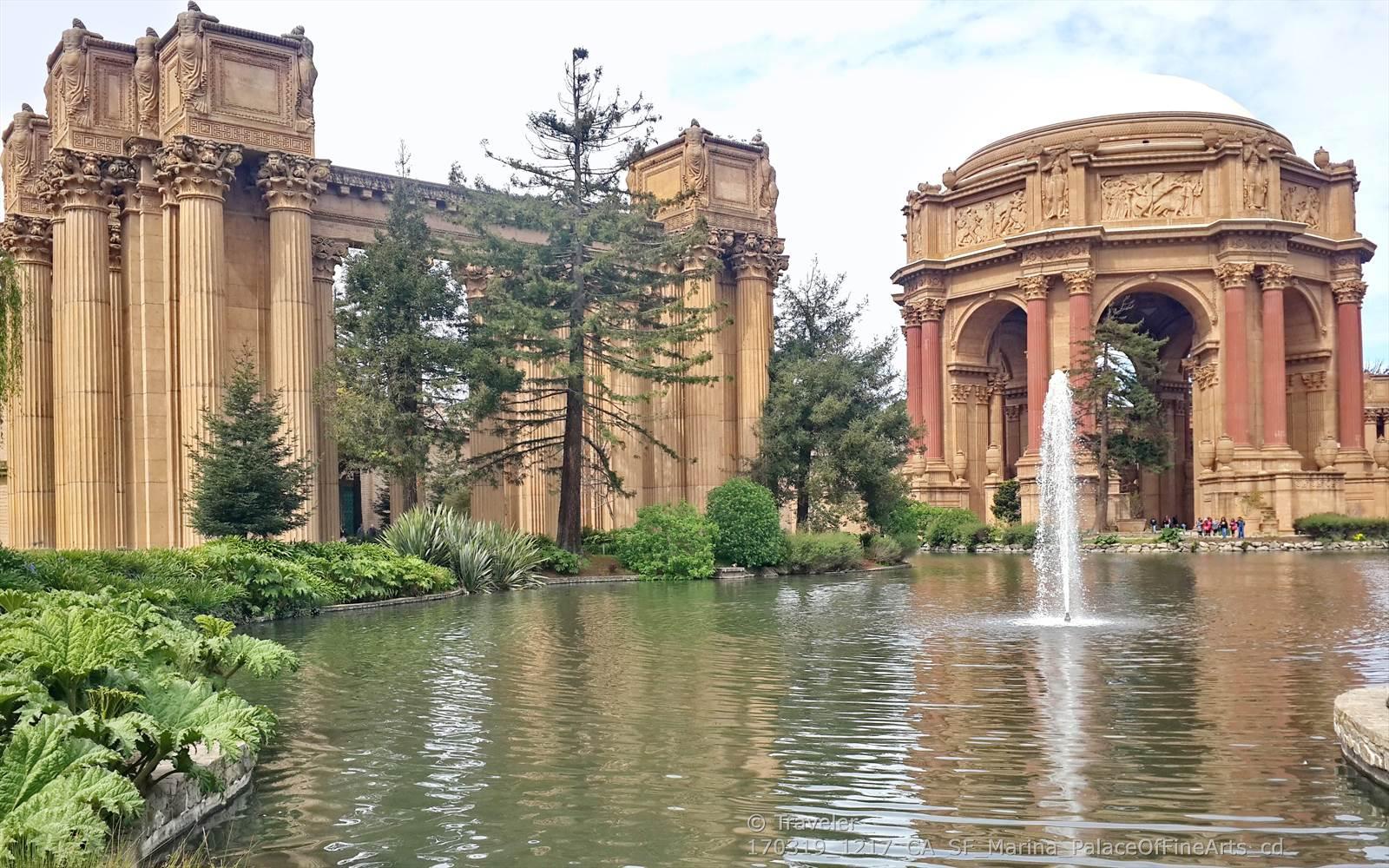 Ornate classical buildings beside a pond with a fountain, bright daylight.