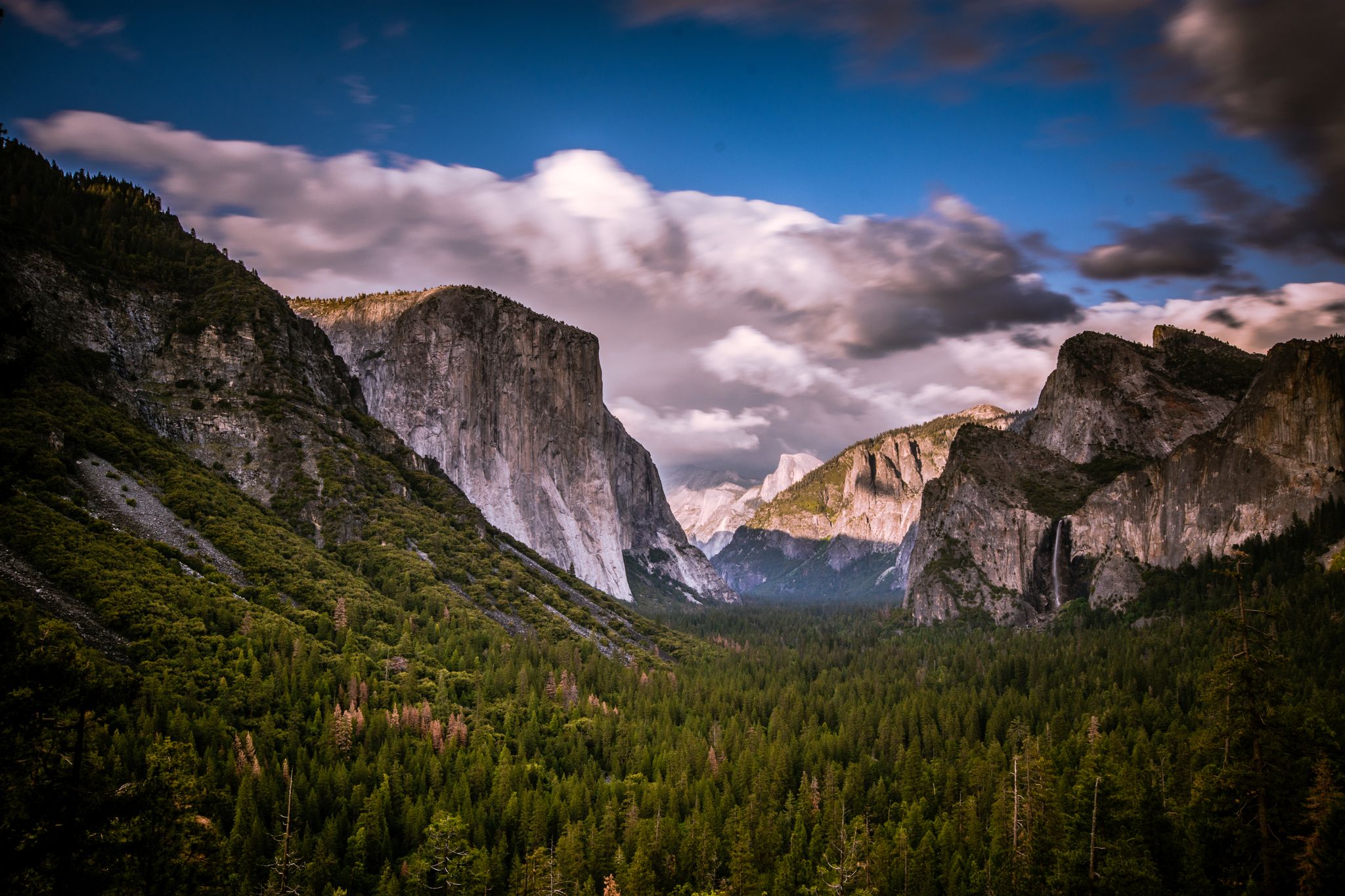 Dramatic valley view with massive rock walls, a waterfall, and dense green forest. - Glacier Point Trailhead – View of Yosemite Valley loop from Badger Pass Ski Area