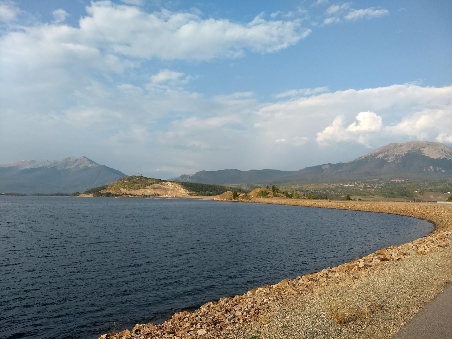 Expansive lake with curved rocky shore and mountains under a cloudy sky.