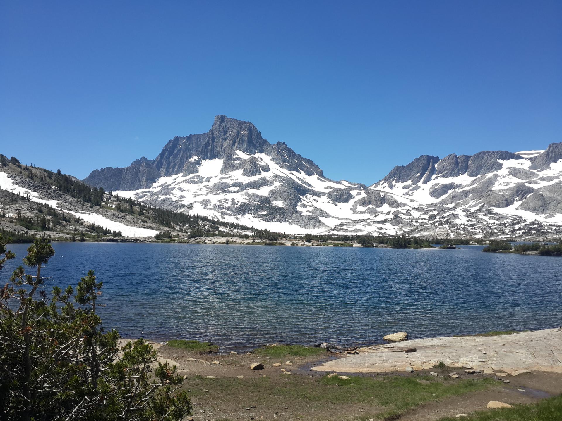 Clear blue lake reflecting snow-capped mountains under a bright sunny sky.