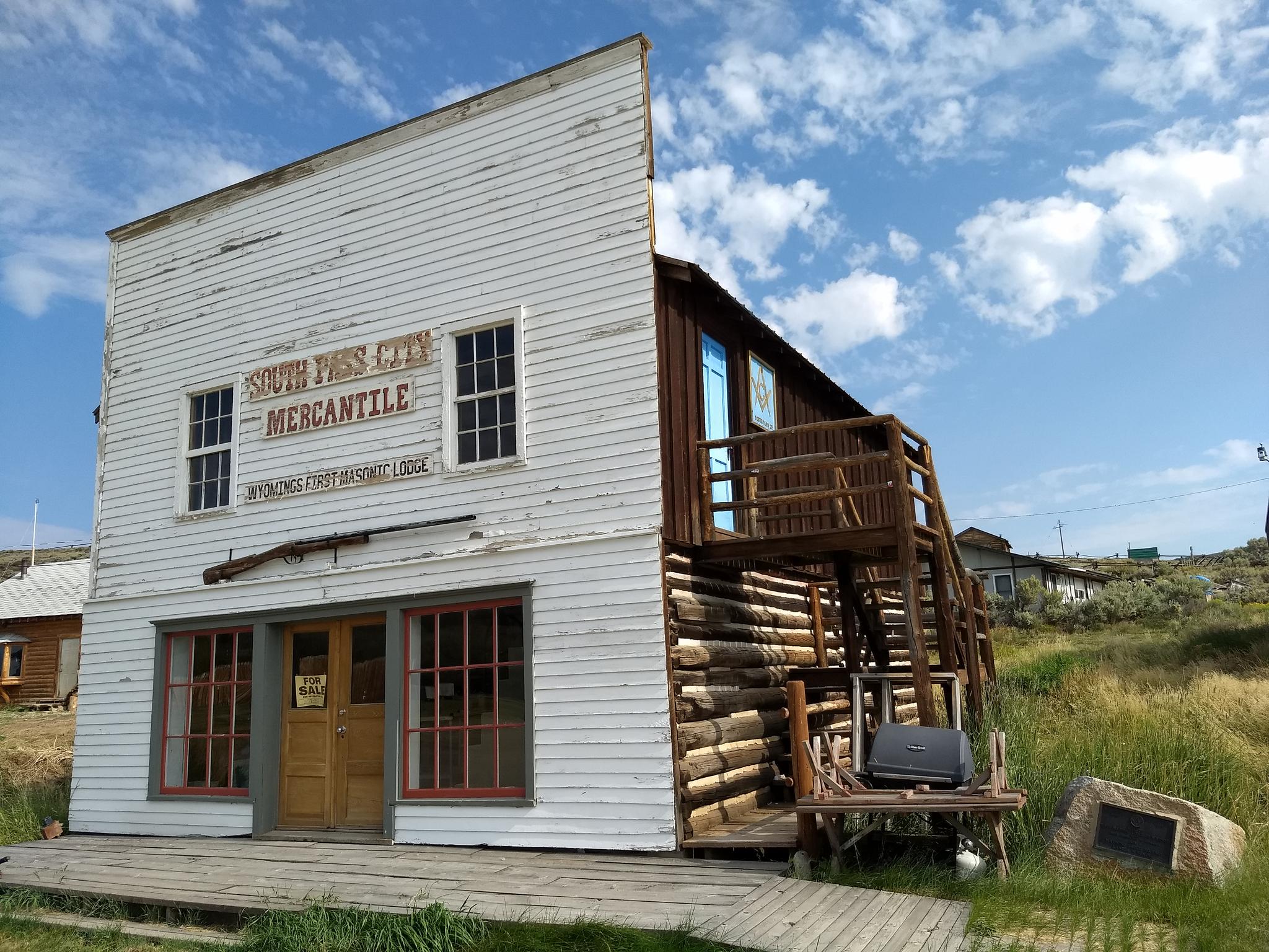 Old white mercantile building with rustic wooden side, under a bright, cloudy sky.