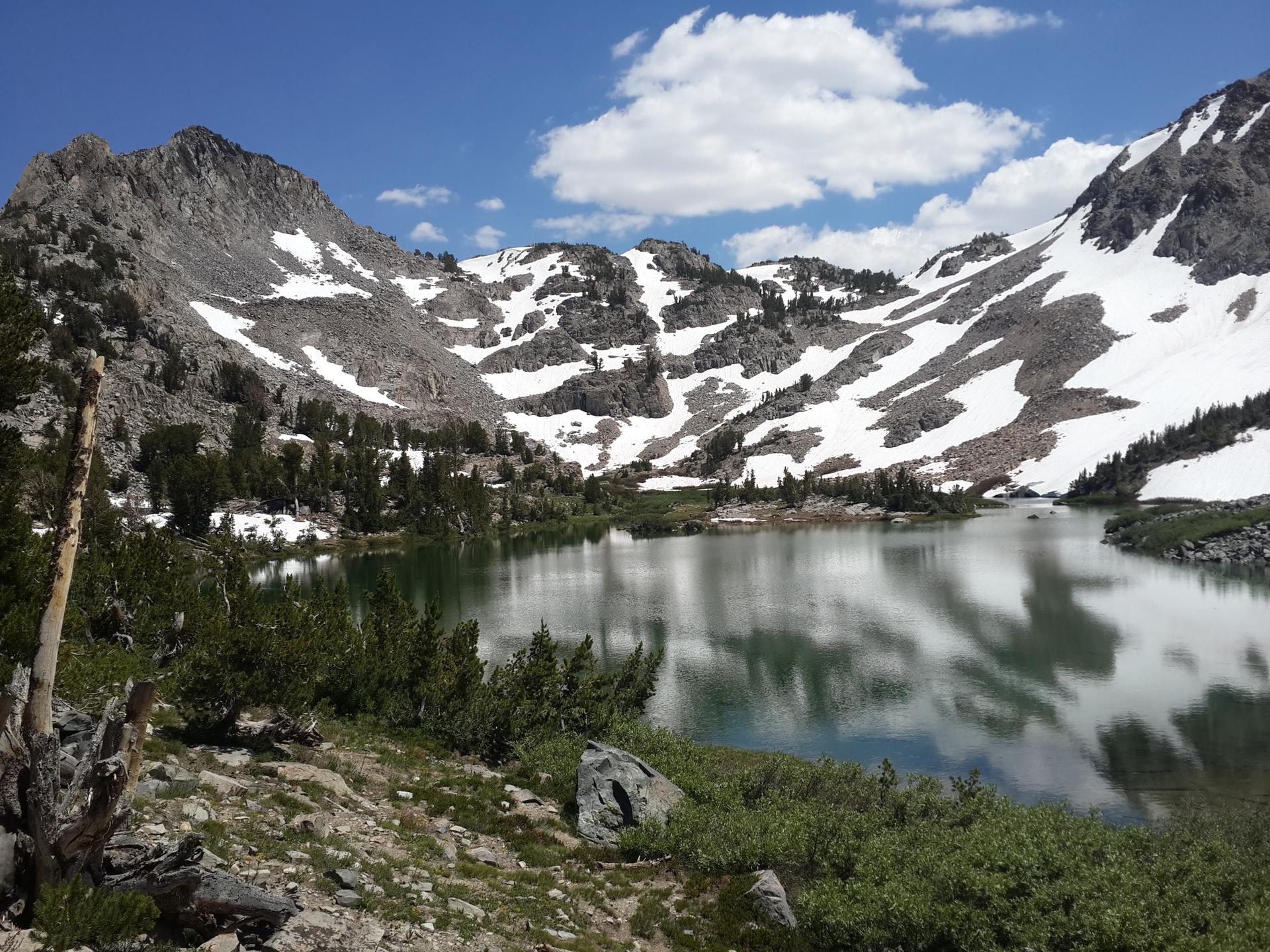 A calm lake reflecting snow-capped mountains and a partly cloudy sky.